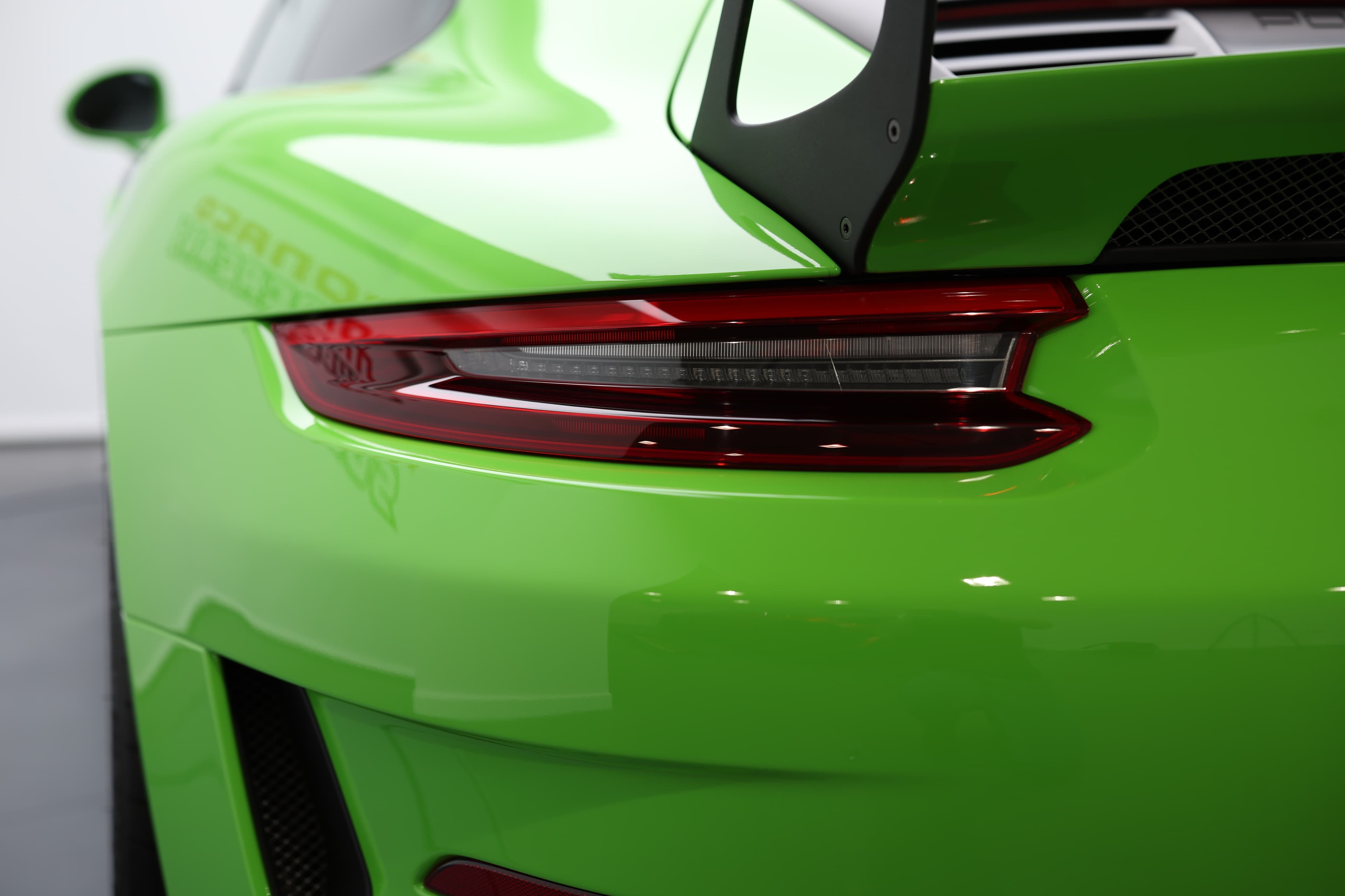 Vue arrière d’une voiture de sport verte, mettant en valeur le feu arrière et l’aileron pour un design sportif et hautes performances.