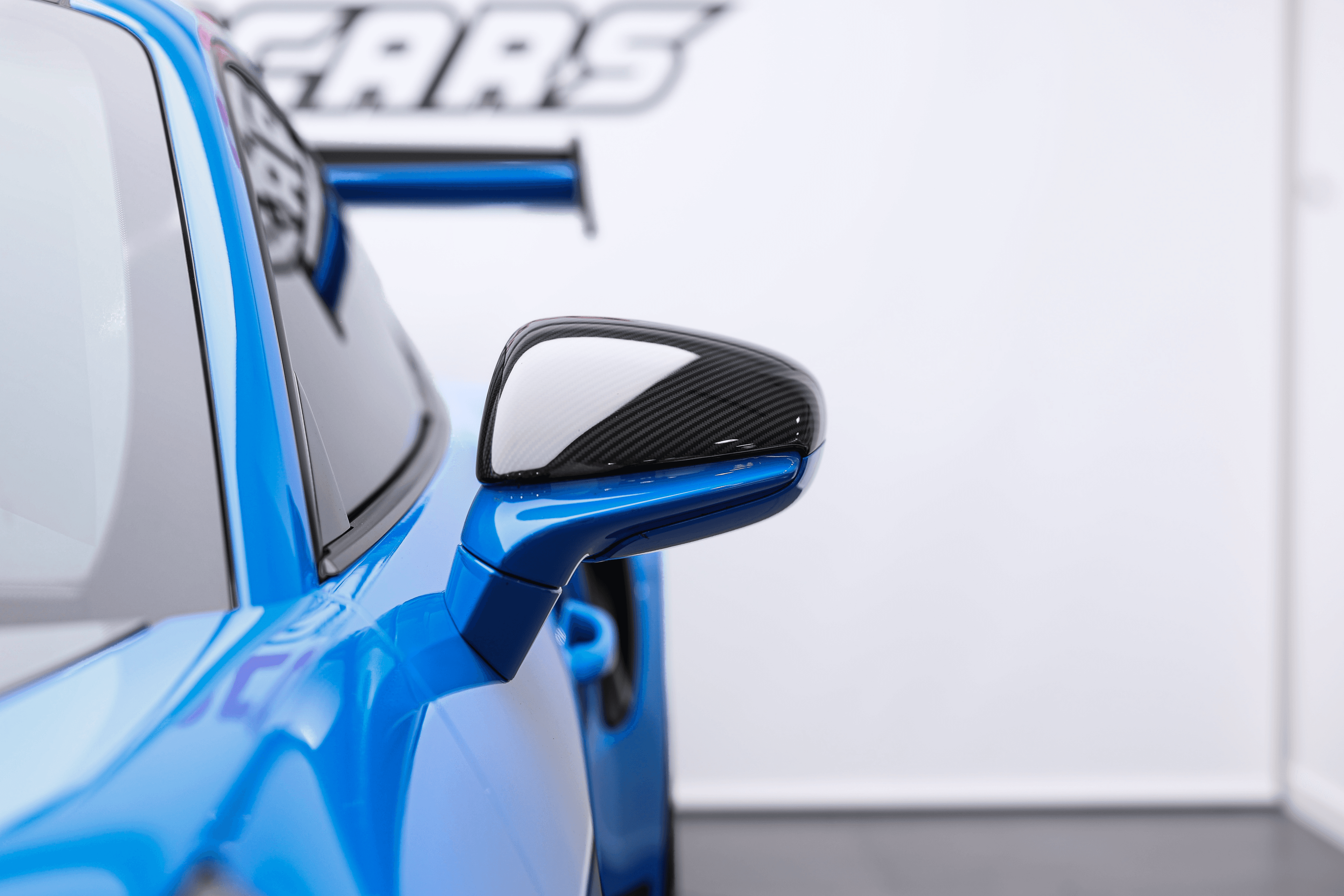 Zoom sur le rétroviseur en carbone de la Porsche GT3RS bleue dans notre showroom à Monaco, un détail qui accentue son allure sportive et moderne.