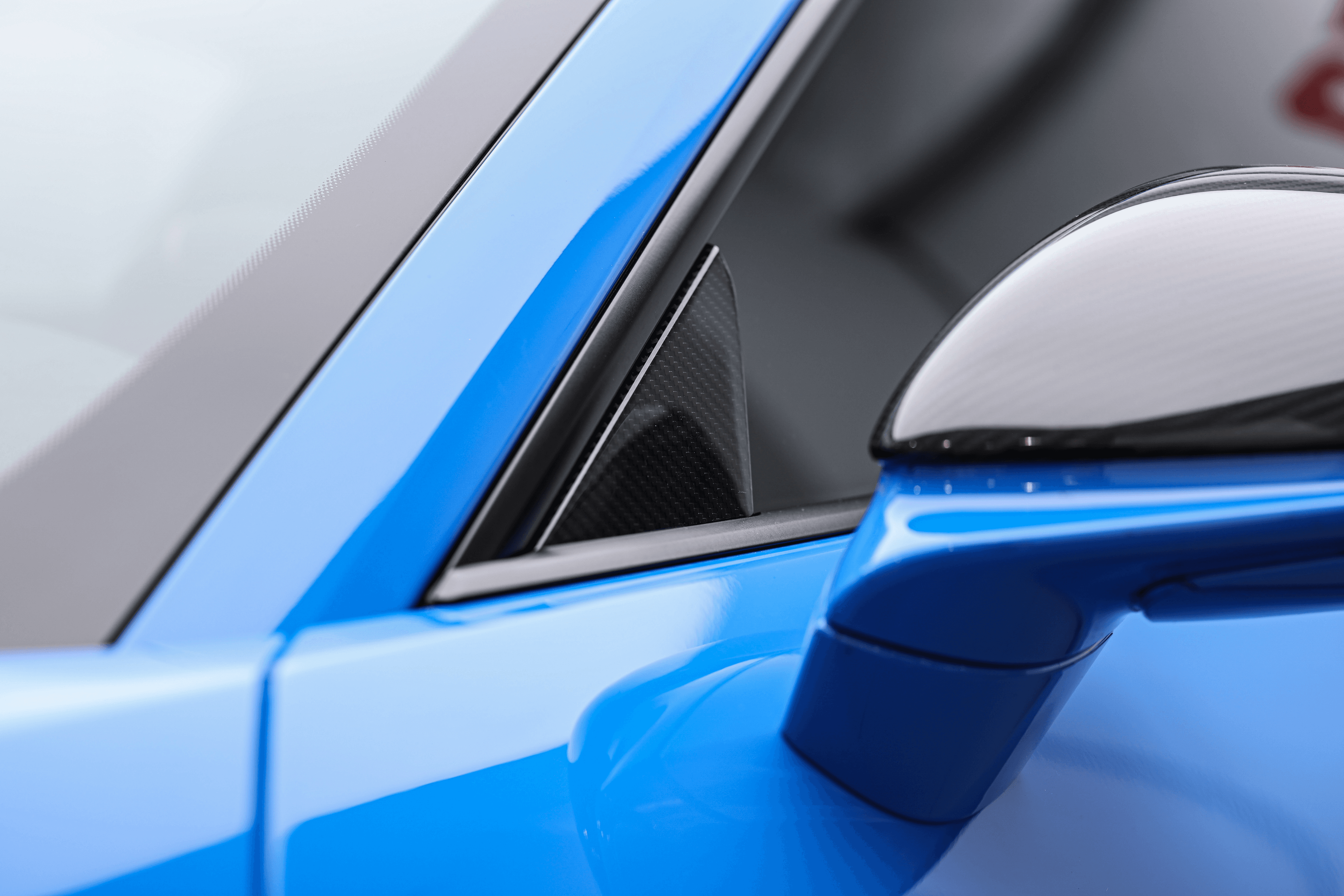 Focus sur le détail aérodynamique du rétroviseur de la Porsche GT3RS bleue dans notre showroom à Monaco, mettant en avant son design raffiné et fonctionnel.