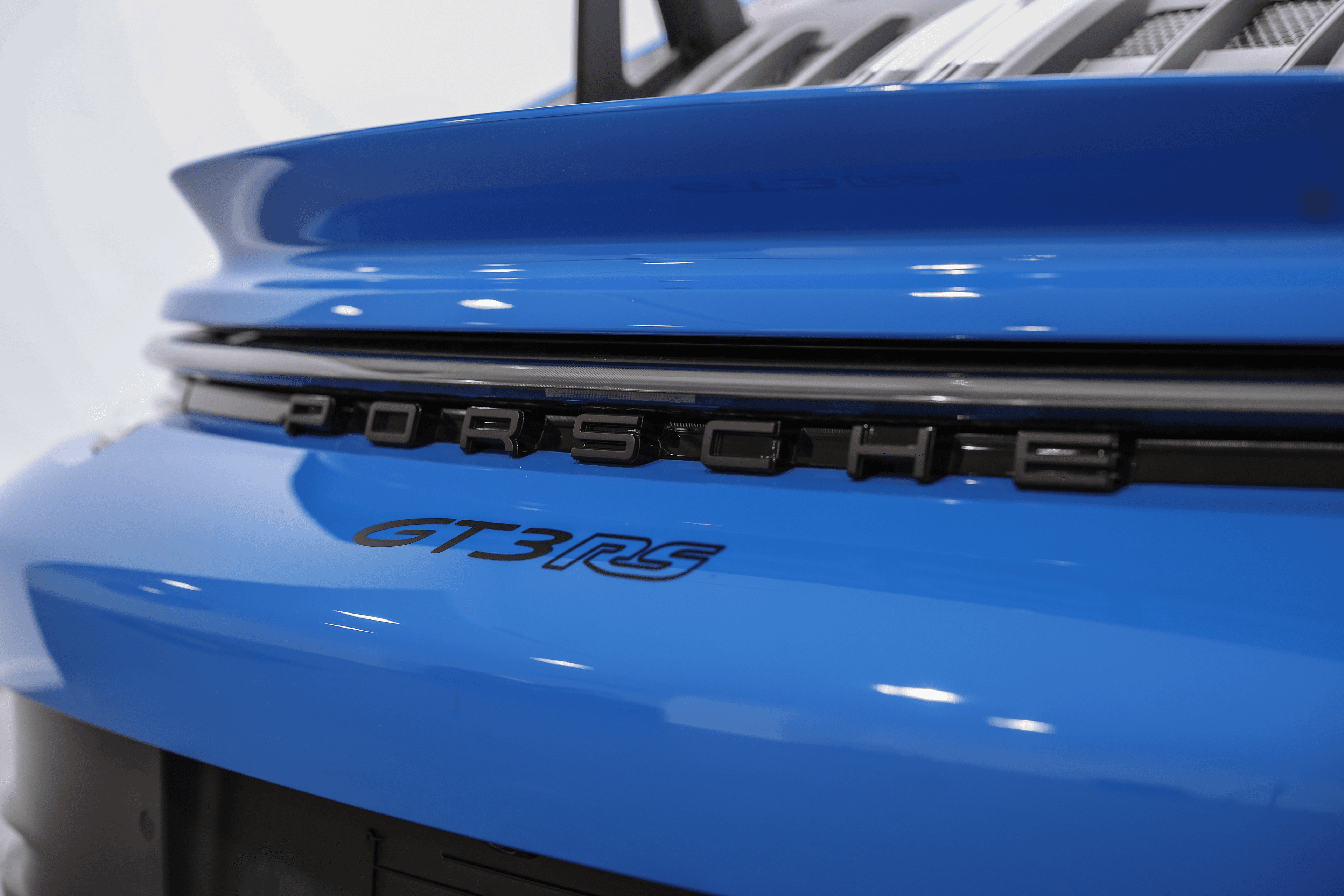 Zoom sur le badge emblématique de la Porsche GT3RS bleue, soulignant l'identité et l'héritage de la marque, tout en mettant en avant le design raffiné de la carrosserie.