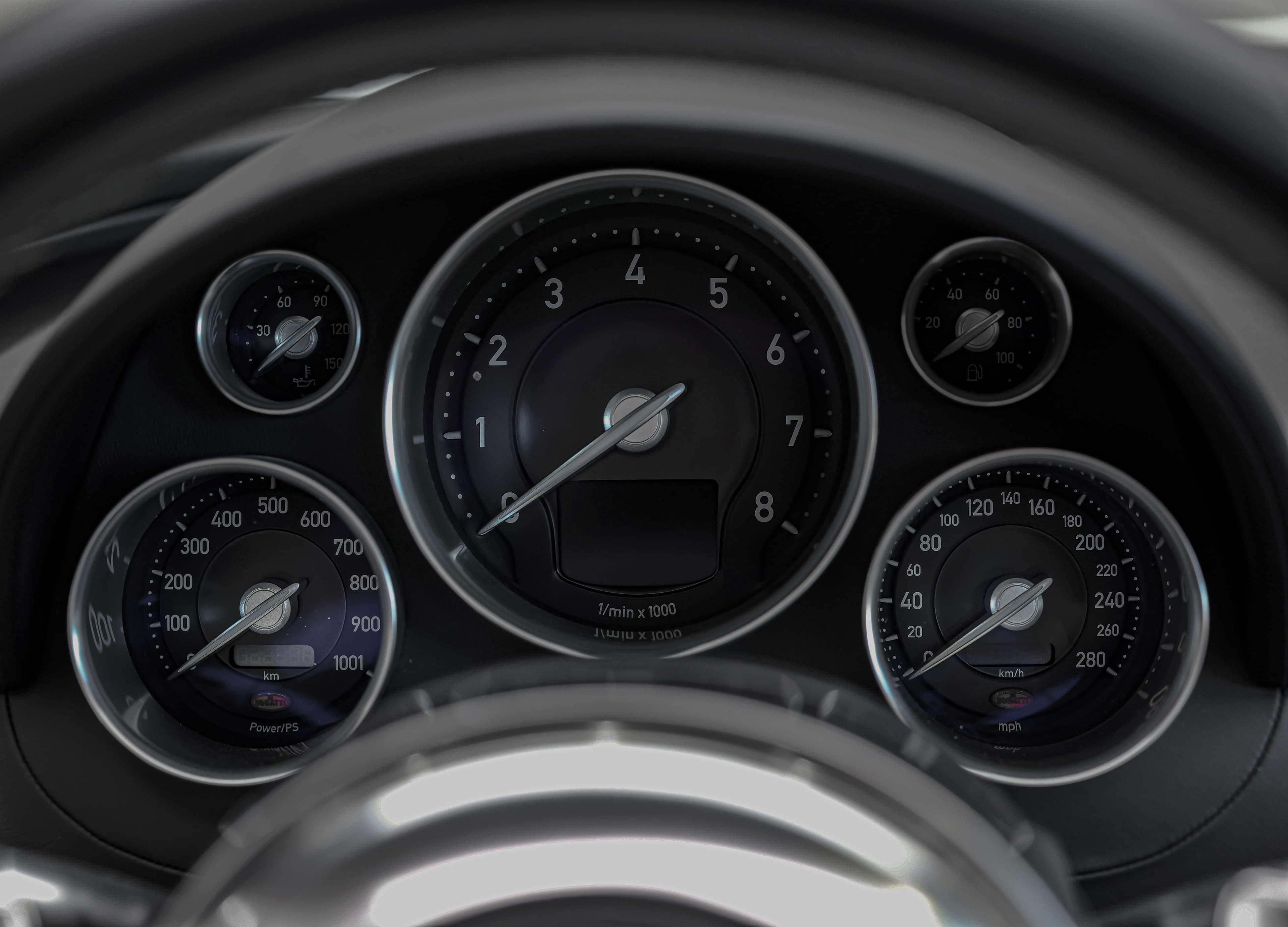 Le tableau de bord de la Bugatti Veyron, visible derrière le volant, présente une série de compteurs numériques et analogiques, alliant élégance et technologie, offrant au conducteur un aperçu précis de la performance et de la puissance de la voiture.