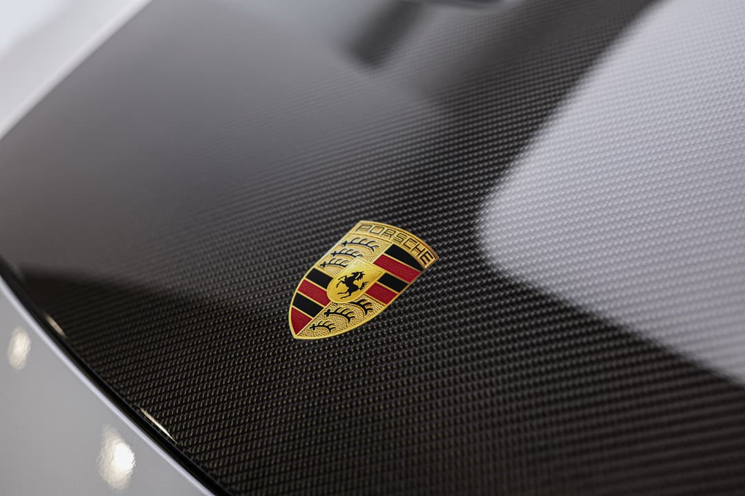 Cette image du logo Porsche, emblématique et reconnaissable, symbolise l'héritage de performance et de luxe de la marque, avec son design distinctif mêlant les couleurs noir, rouge et or, ainsi que le blason du cheval cabré.