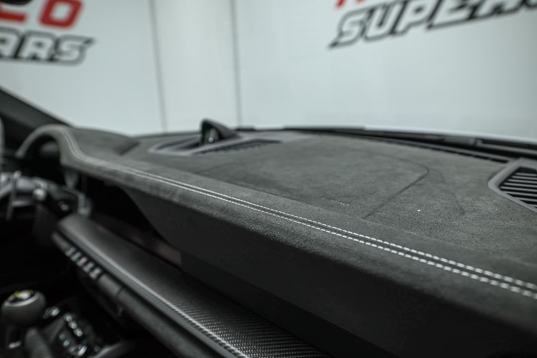 Cette image du tableau de bord en Alcantara de la Porsche 911 GT3 RS souligne le luxe et la sportivité, offrant une texture agréable au toucher tout en améliorant l'adhérence et le style, pour une expérience de conduite à la fois raffinée et dynamique.