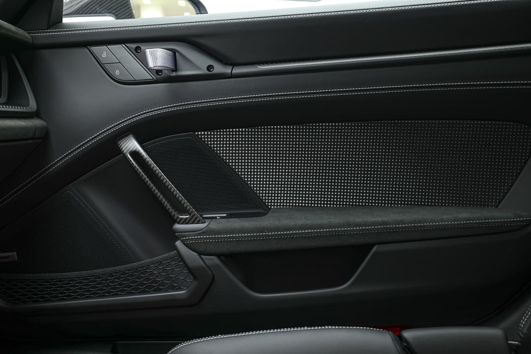 L'image montre l'intérieur de la porte d'une Porsche, mettant en avant un poignet en carbone et une ouverture de poutre en tissu, soulignant le mélange de luxe et de sportivité dans le design.