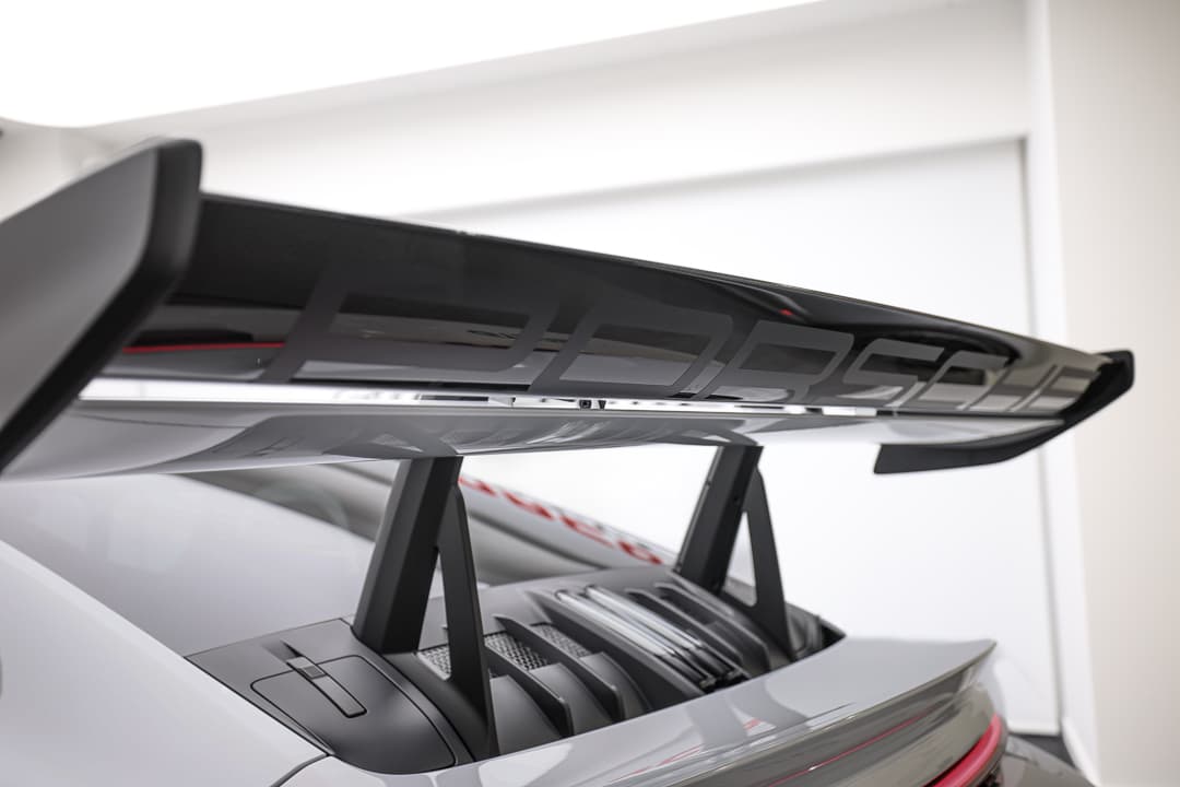 Aileron Porsche, design aérodynamique, inscription Porsche, performance automobile, luxe, sportivité, détails raffinés.