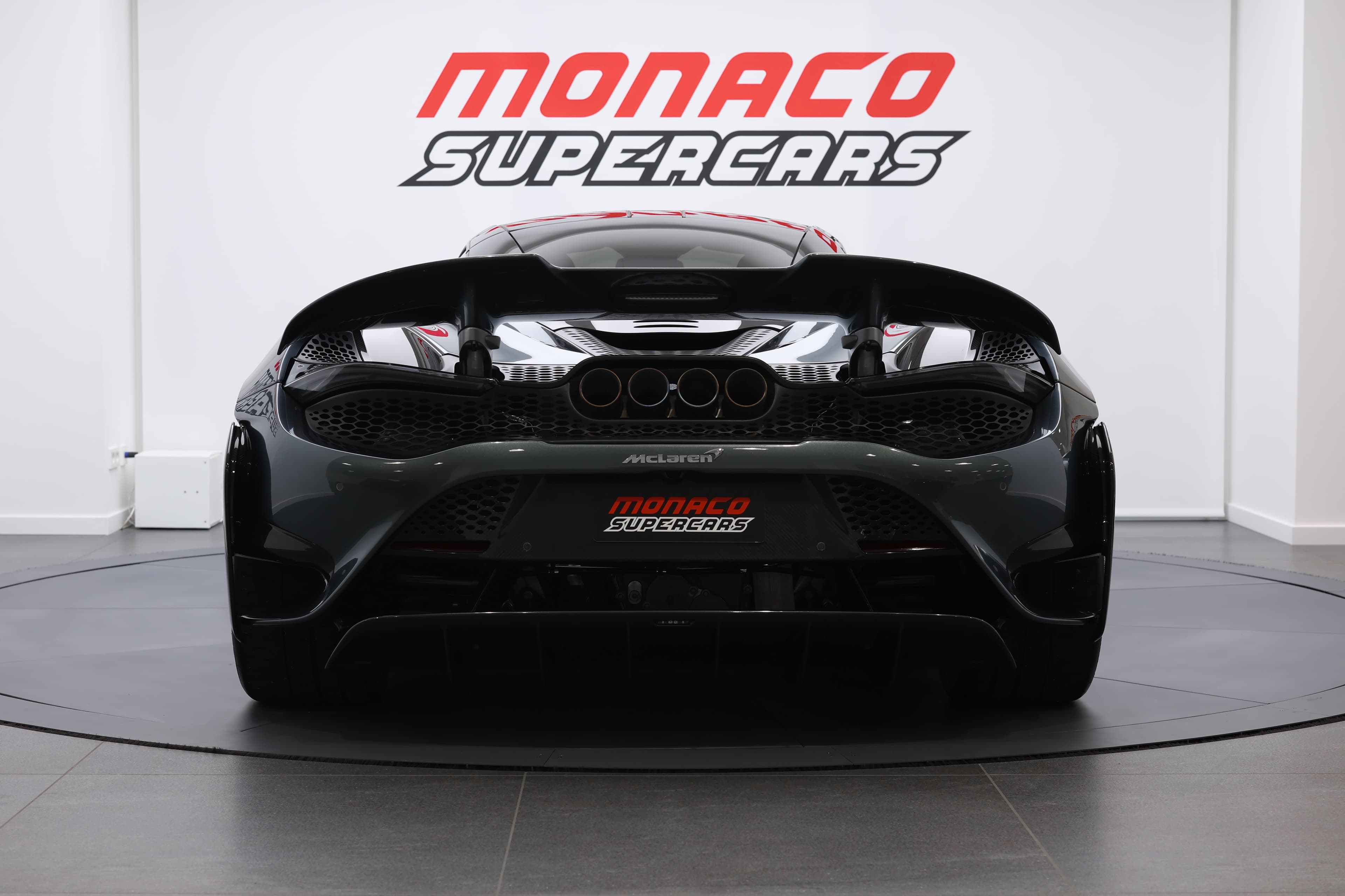 L'image présente l'arrière d'une McLaren 765LT, mettant en avant ses feux arrière angulaires, le diffuseur sport et l'échappement central, soulignant son look agressif et sa technologie avancée.