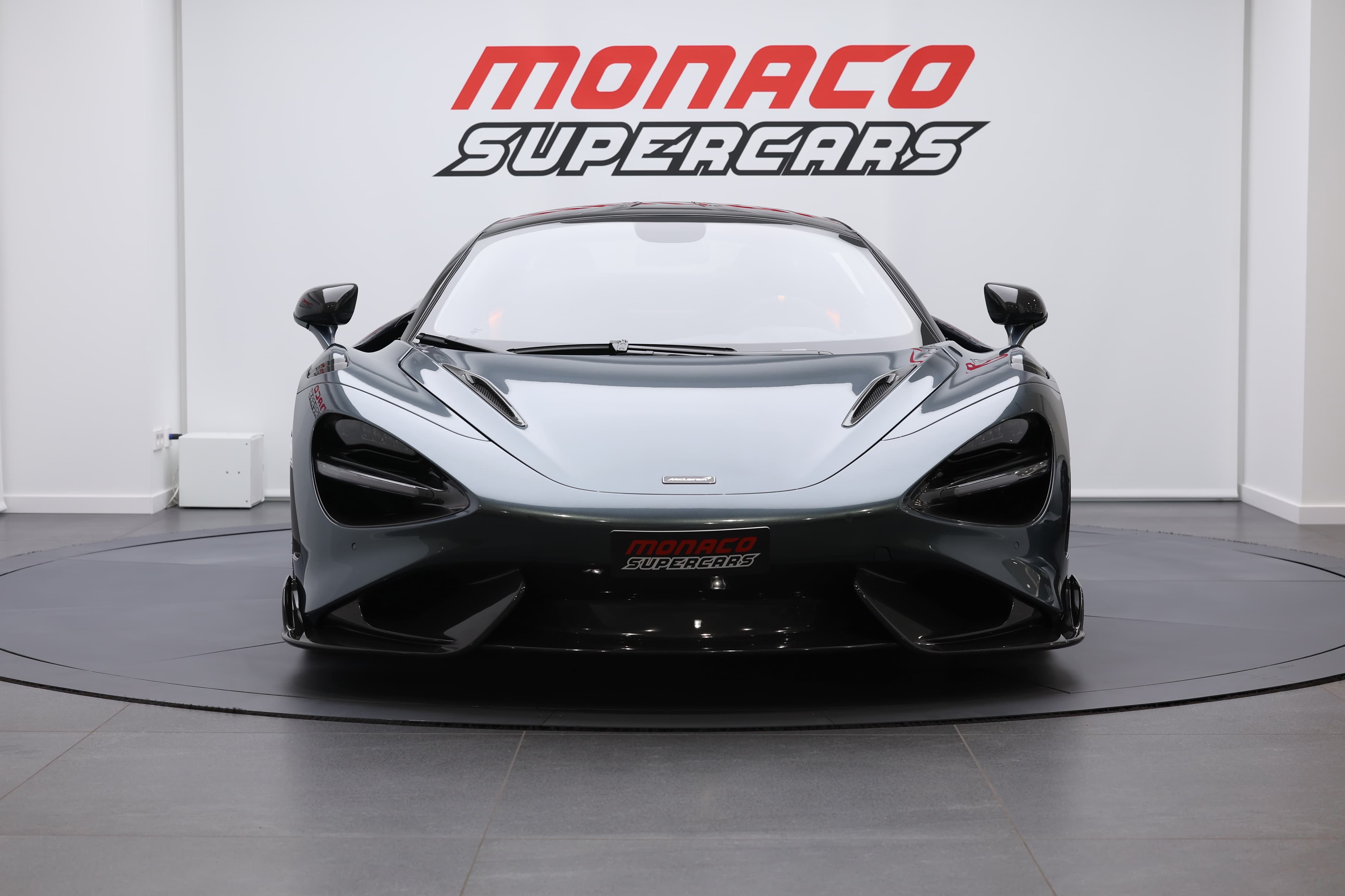 L'image présente l'avant d'une McLaren 765LT, mettant en avant sa calandre distinctive, ses phares modernes et le design agressif du pare-chocs, soulignant son allure dynamique et son esprit de performance.