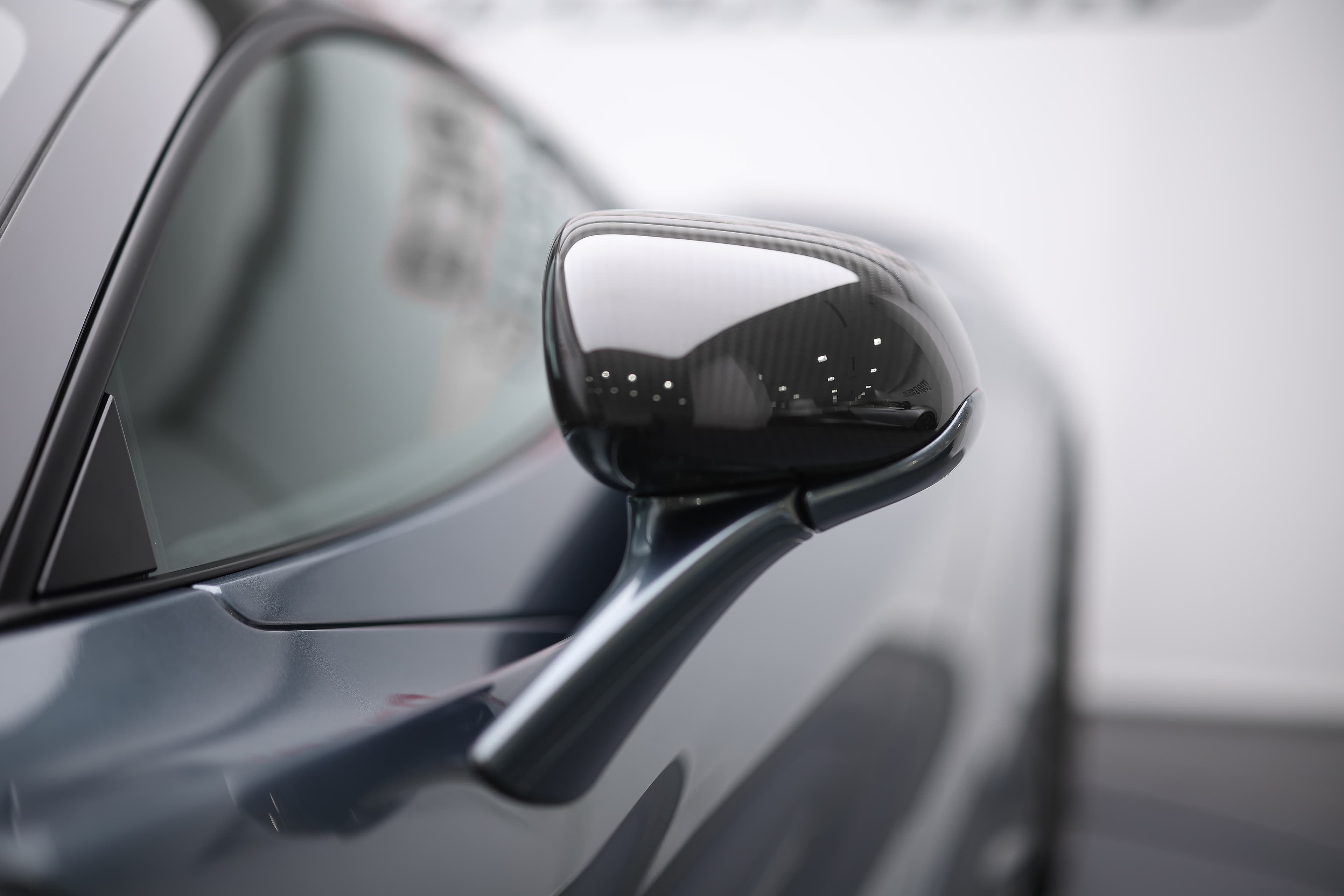 L'image met en avant le rétroviseur en carbone de la McLaren 765LT, soulignant son design aérodynamique et léger, ainsi que la finition haut de gamme qui ajoute une touche sportive à l'ensemble du véhicule.