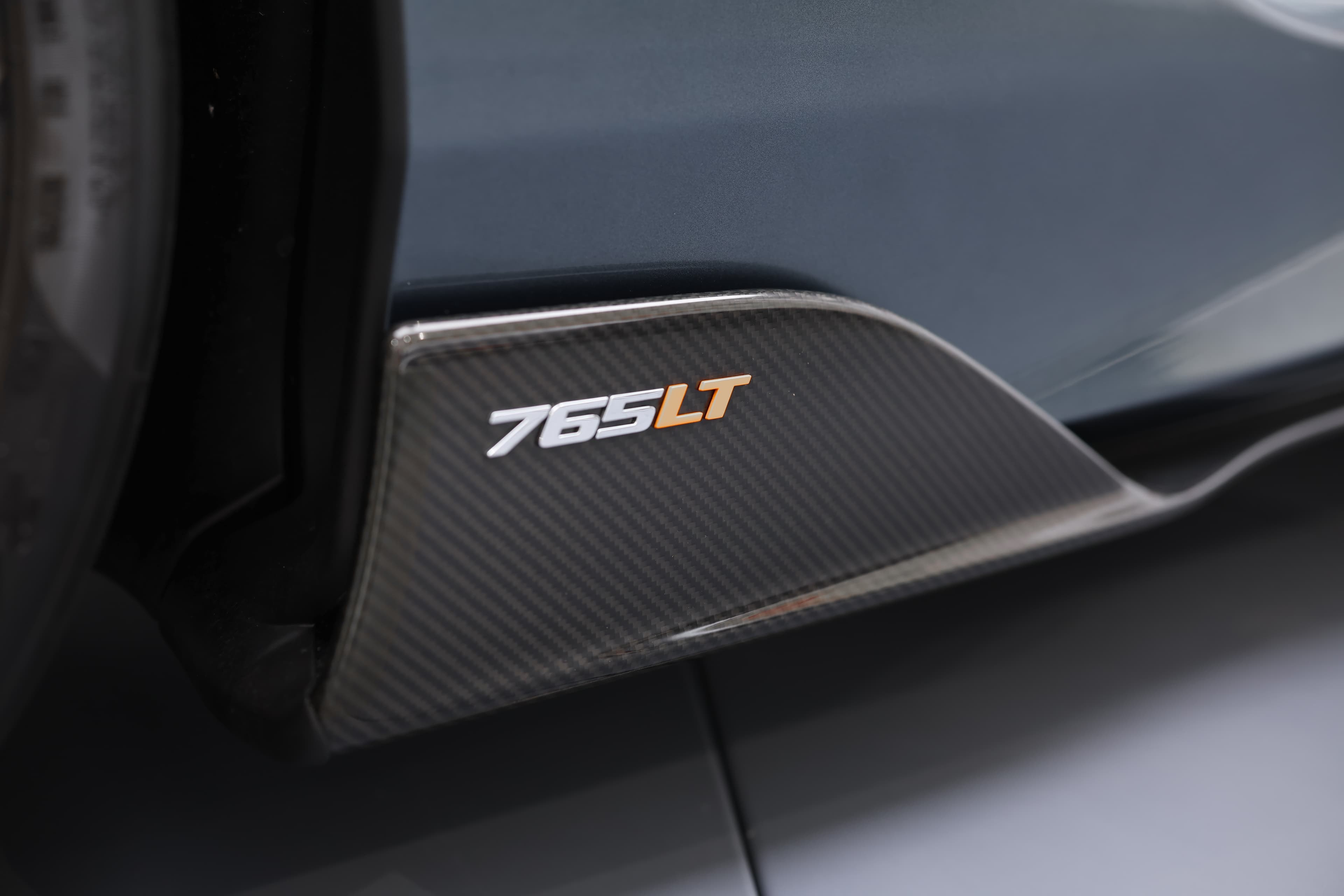 L'image montre la lame en carbone de la McLaren 765LT, mettant en avant son design aérodynamique et agressif, qui améliore la stabilité et l'adhérence à haute vitesse tout en ajoutant un élément visuel saisissant à l'avant de la voiture.