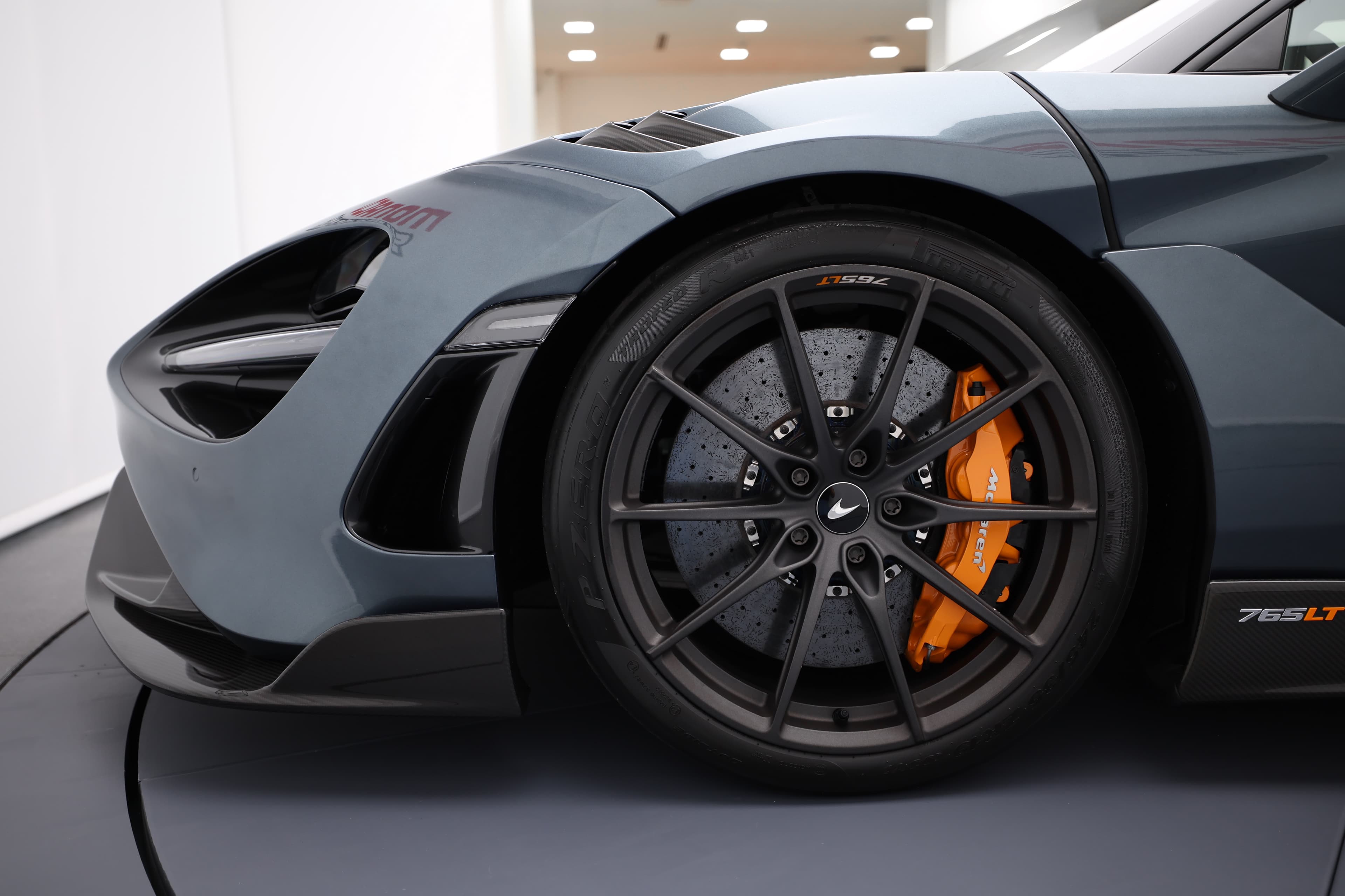 L'image montre la moitié avant de profil de la McLaren 765LT, mettant en avant ses lignes aérodynamiques, son capot sculpté et ses phares distinctifs, qui soulignent le caractère sportif et agressif de la voiture.