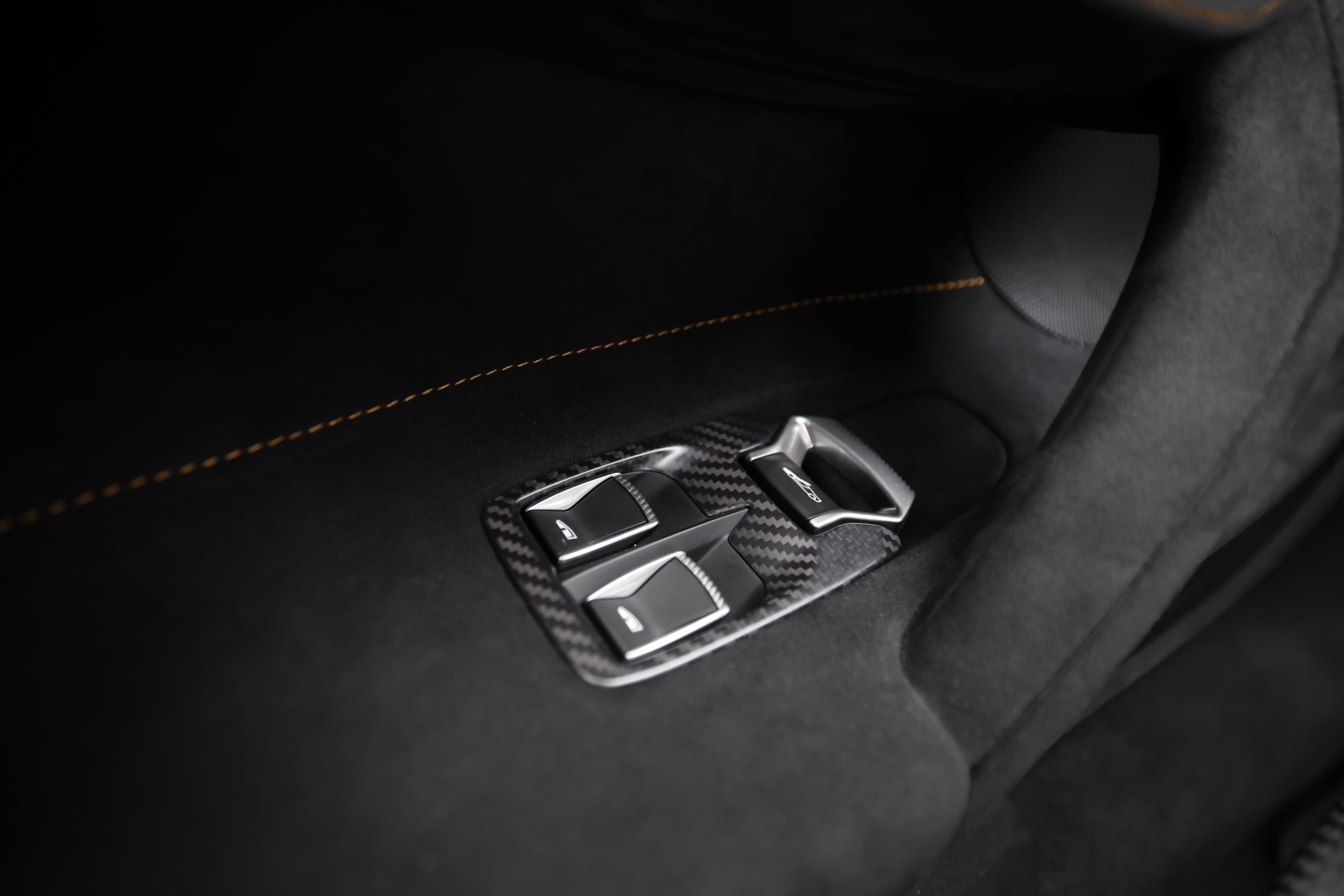 L'image met en avant un bouton de contrôle des vitres, entouré de fibre de carbone, soulignant le mélange de fonctionnalité et de luxe. Le matériau carbone ajoute une touche sportive et haut de gamme à l'intérieur du véhicule, reflétant l'orientation vers la performance de la marque.