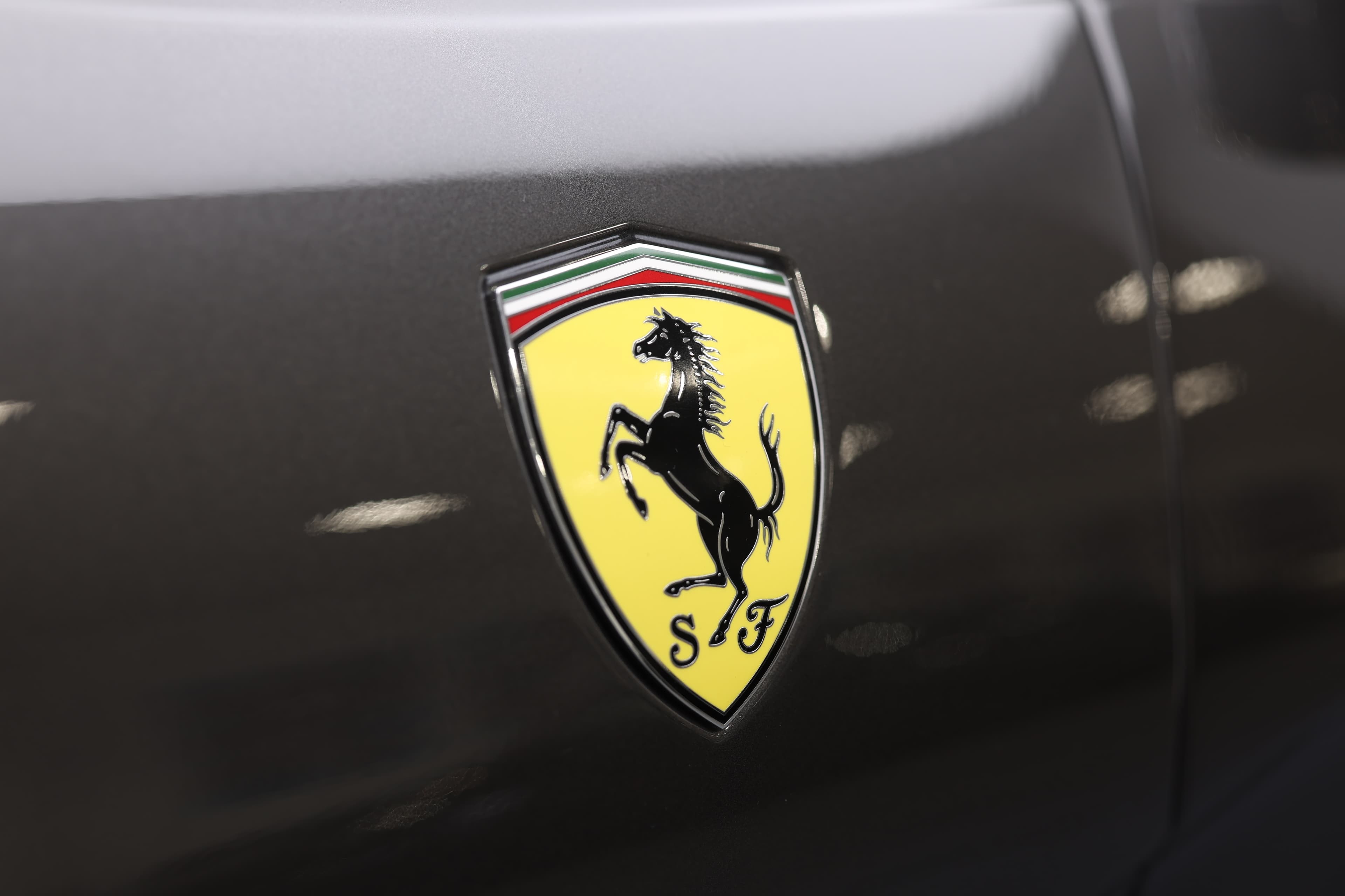 Le logo Ferrari est emblématique, représentant un cheval cabré noir sur fond jaune, entouré de la lettre "S" pour "Scuderia". Ce symbole incarne l'esprit de compétition, la vitesse et l'héritage de la marque italienne.