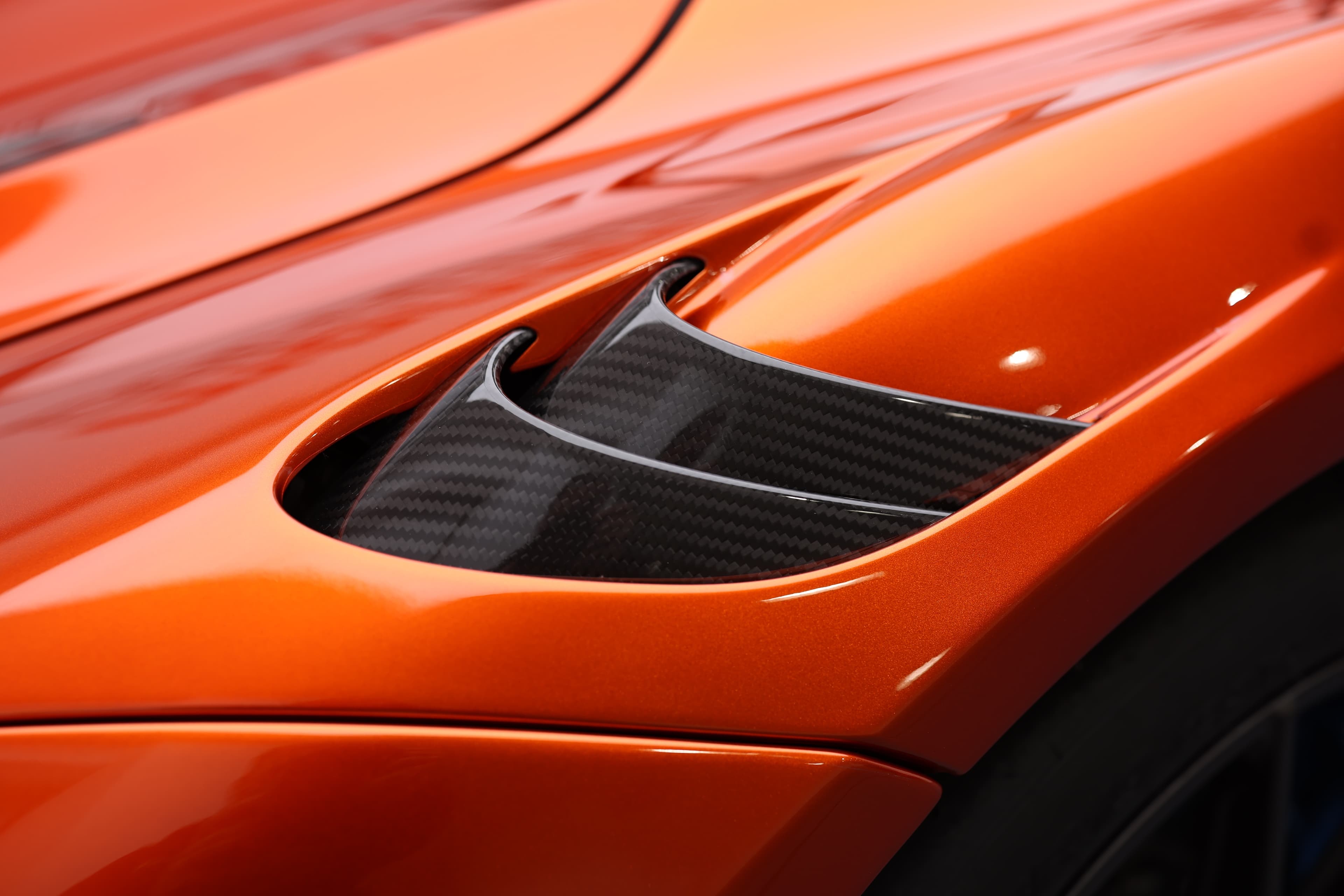 Gros plan sur une prise d'air de la McLaren 765LT, mettant en avant le design aérodynamique et les détails en carbone, illustrant l'importance de la performance et de l'efficacité dans le style de cette supercar.