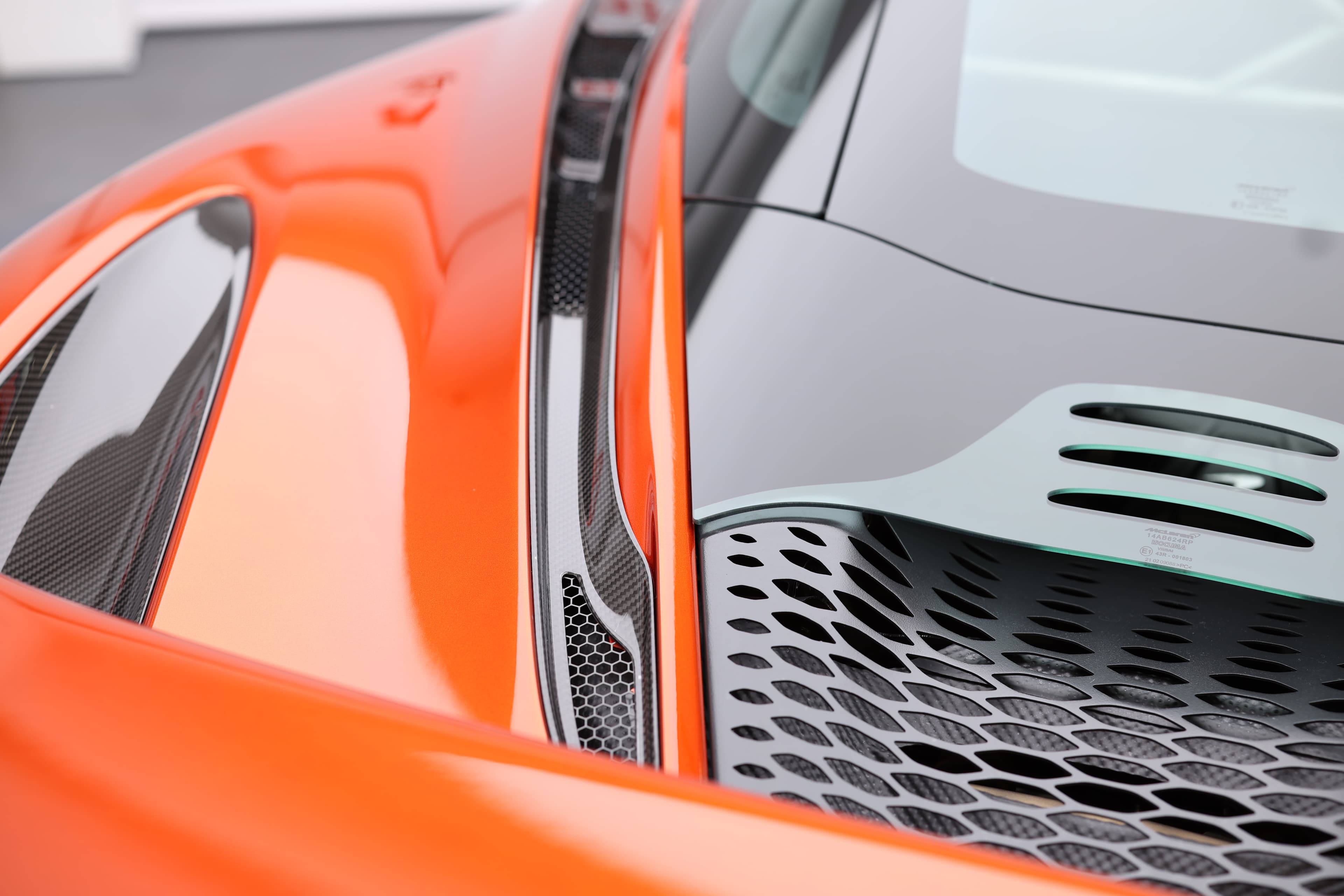 Gros plan sur le détail de la jupe latérale et du capot de la McLaren 765LT, mettant en avant la texture en carbone et le design aérodynamique, illustrant l'harmonie entre performance et esthétique.