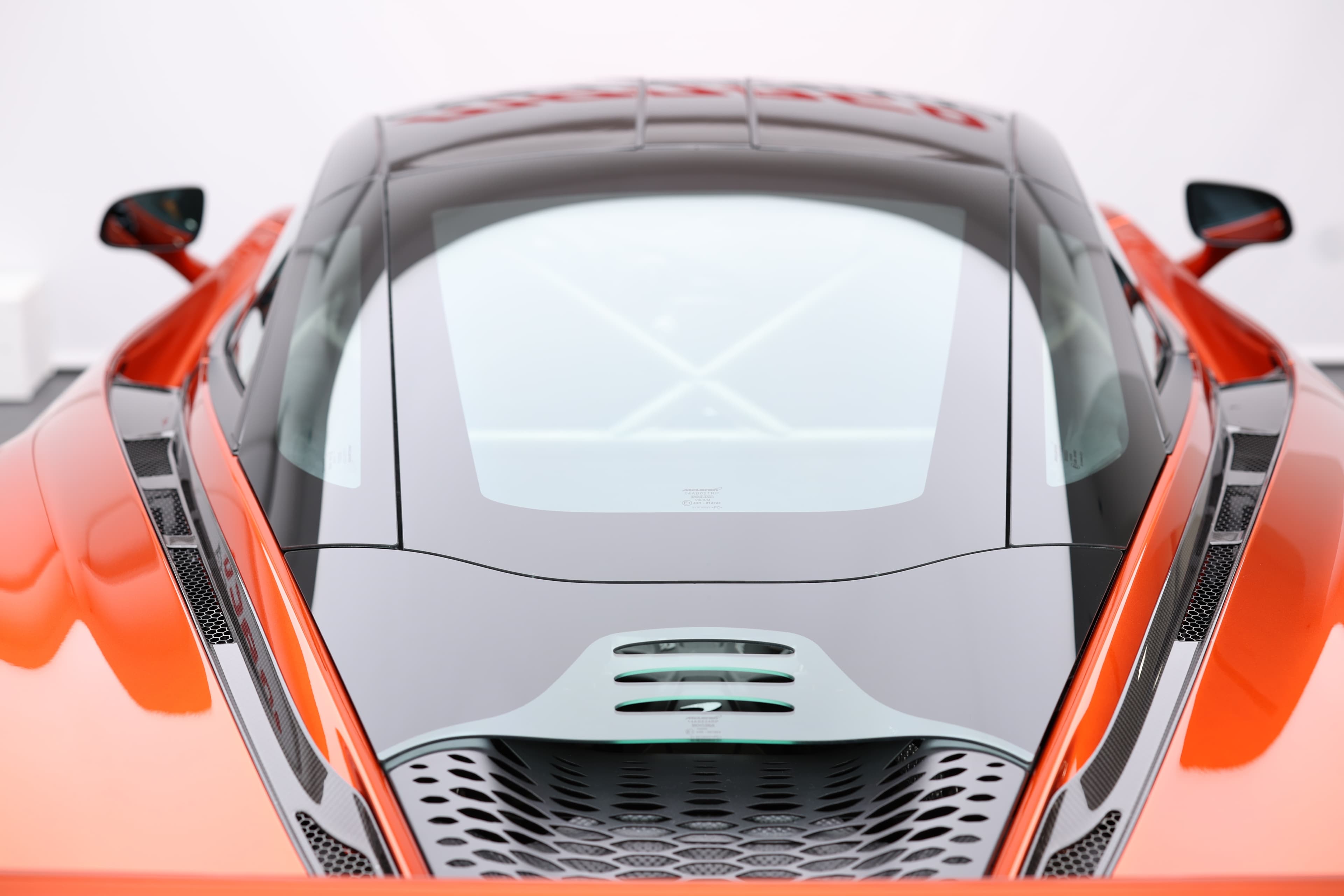 Gros plan sur le toit de la McLaren 765LT, mettant en avant le capot en verre et les éléments aérodynamiques, soulignant l'innovation et le design sophistiqué de cette supercar.