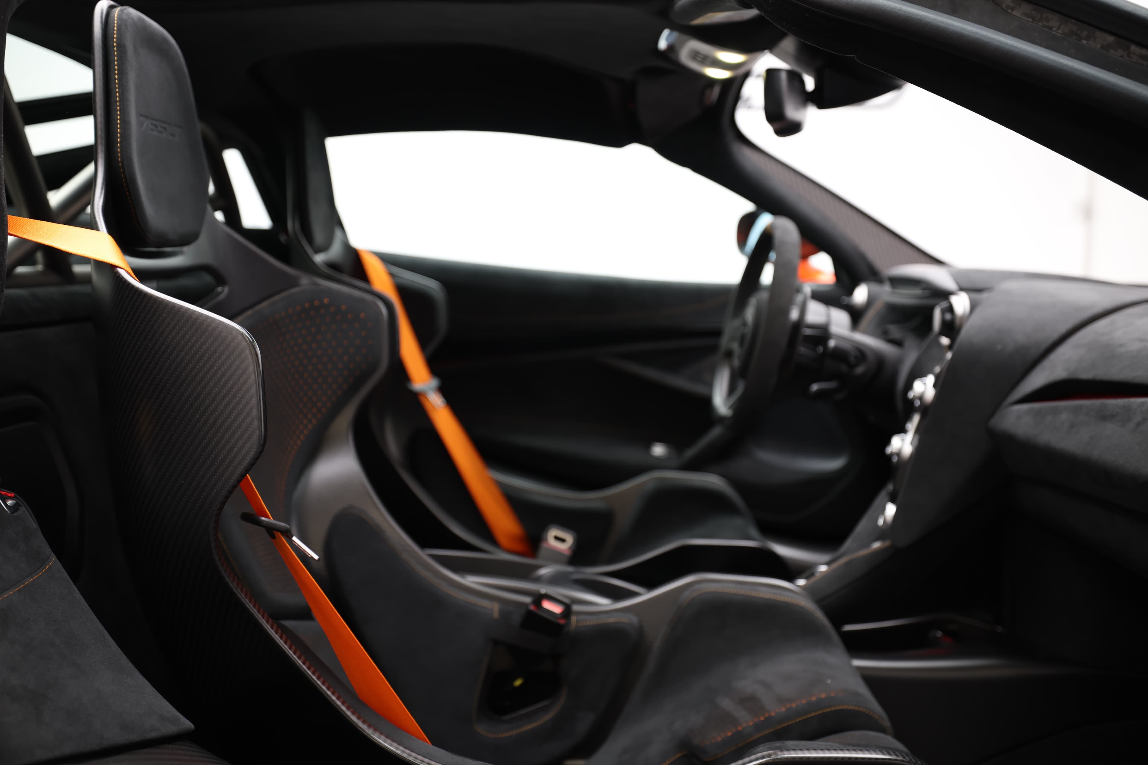 Gros plan sur l'intérieur de la McLaren 765LT, mettant en avant les sièges en carbone, les détails en tissu technique et le tableau de bord, soulignant l'orientation vers la performance et le confort.