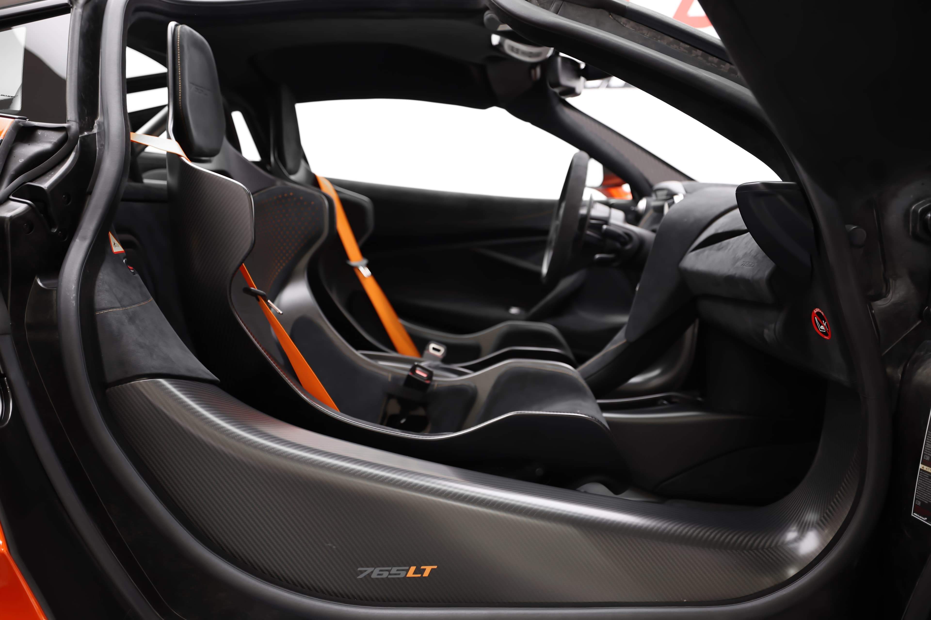 Gros plan sur l'intérieur de la McLaren 765LT, mettant en avant les sièges en carbone, les détails en tissu technique et le tableau de bord, soulignant l'orientation vers la performance et le confort.