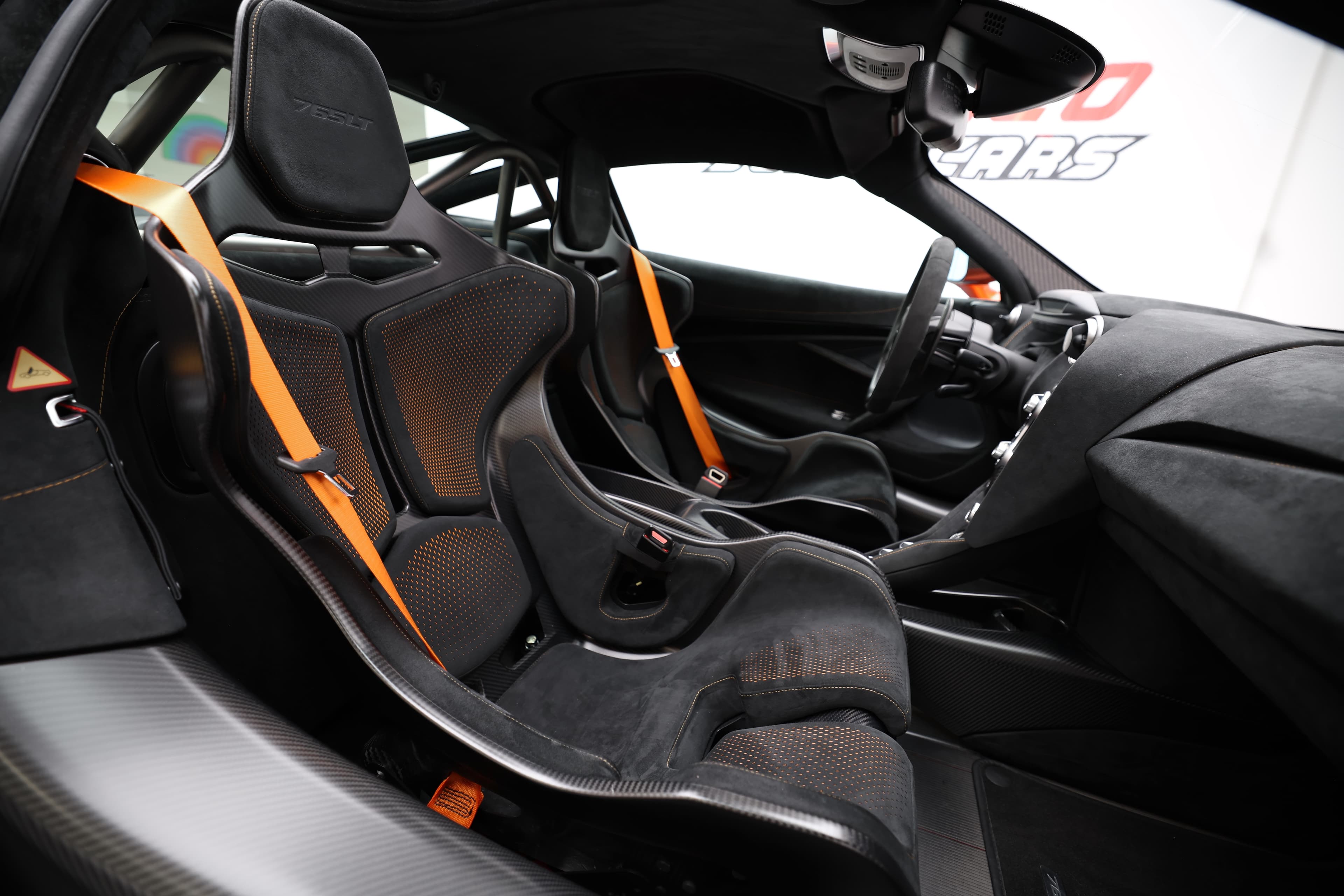 Gros plan sur les sièges en carbone de la McLaren 765LT, mettant en avant les détails de design, les harnais de sécurité et l'intérieur axé sur la performance, illustrant l'engagement envers la course et l'ergonomie.