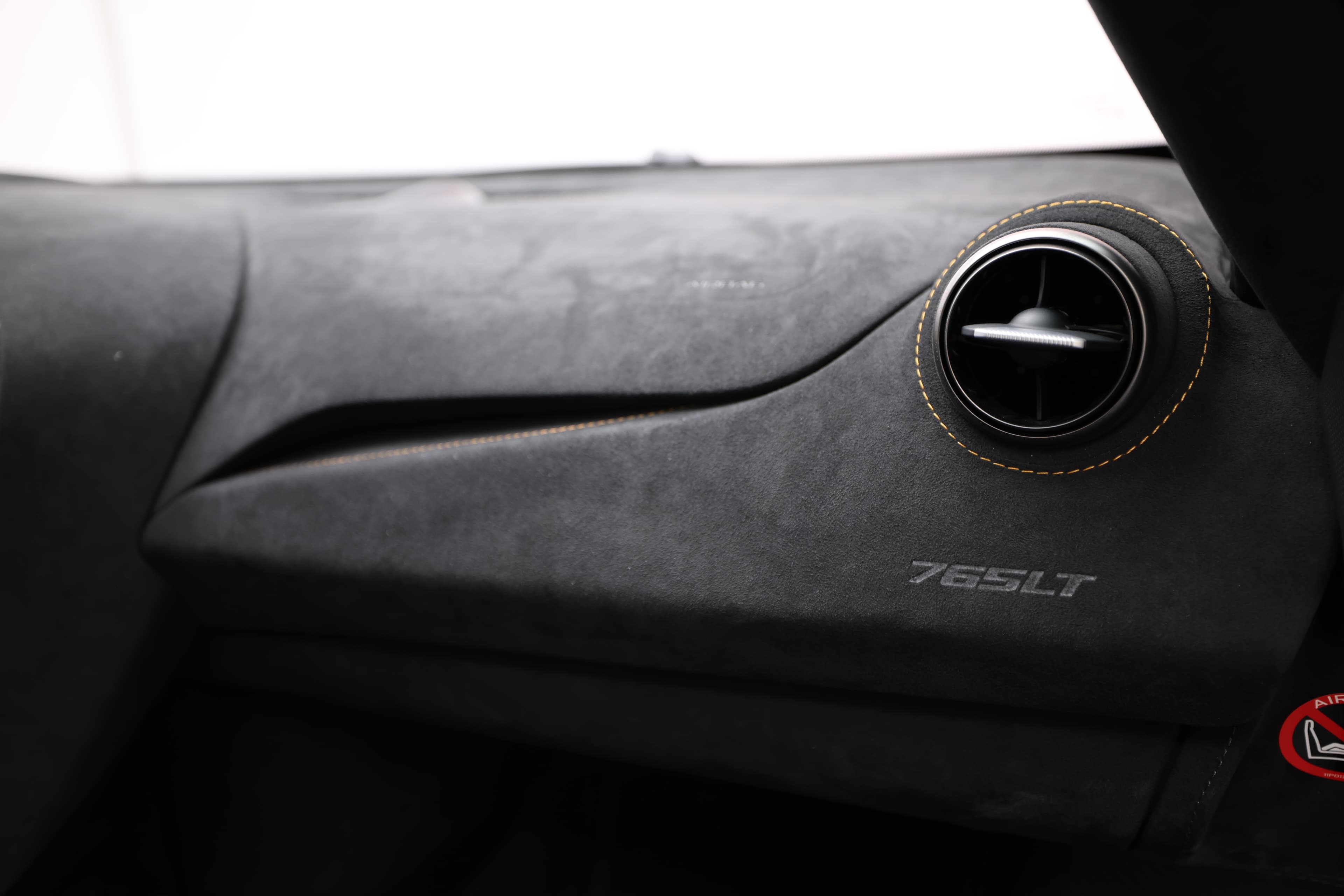 Gros plan sur le tableau de bord de la McLaren 765LT, mettant en avant la texture en carbone et le badge 765LT, symbole de l'ingénierie de pointe et du design minimaliste.