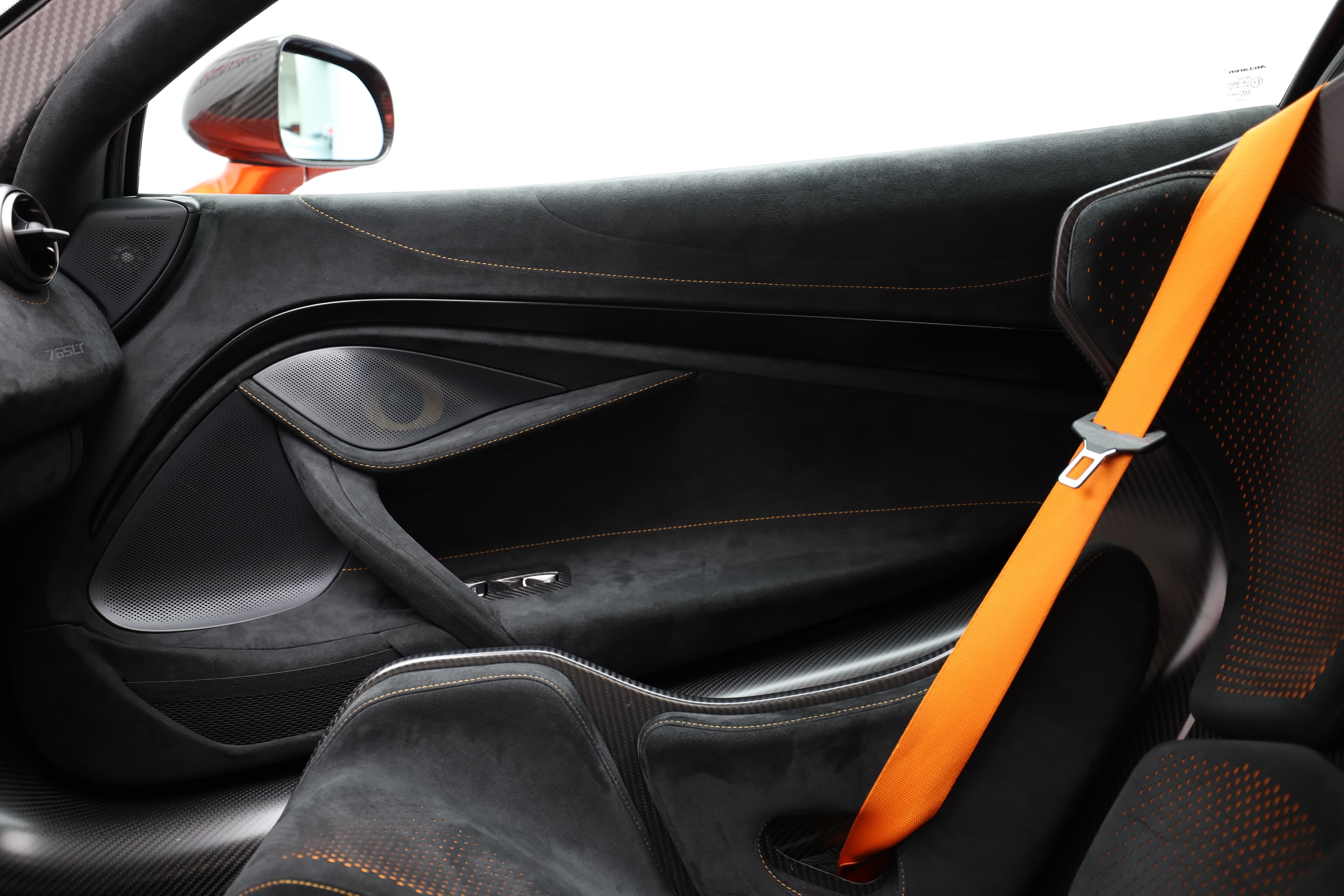 Gros plan sur la ceinture de sécurité orange de la McLaren 765LT, mettant en avant le contraste avec l'intérieur en carbone, soulignant à la fois la sécurité et le style distinctif de la voiture.