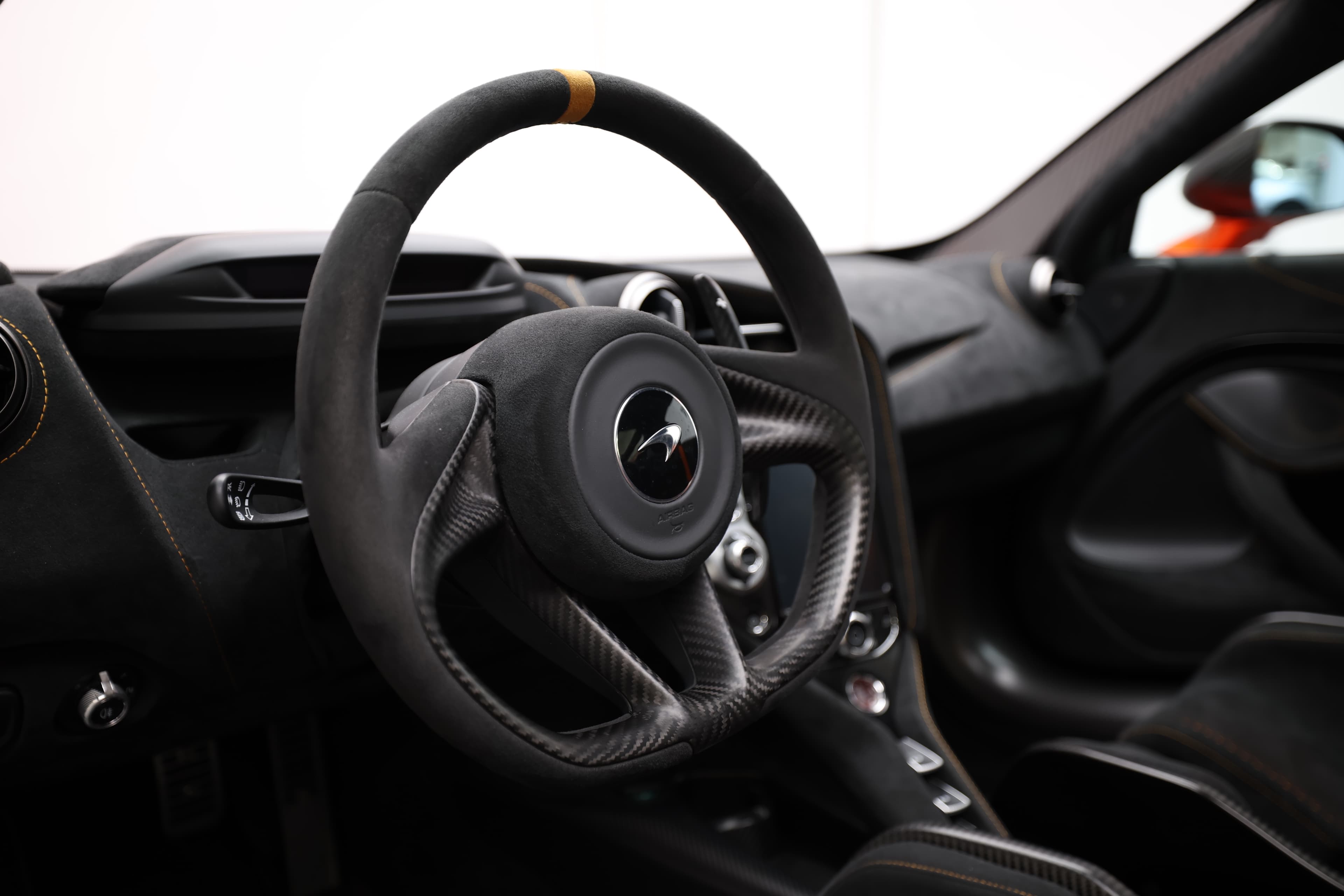 Gros plan sur le volant de la McLaren 765LT, mettant en avant le design ergonomique en carbone et en cuir, ainsi que les commandes intégrées, symbolisant le contrôle et la précision.