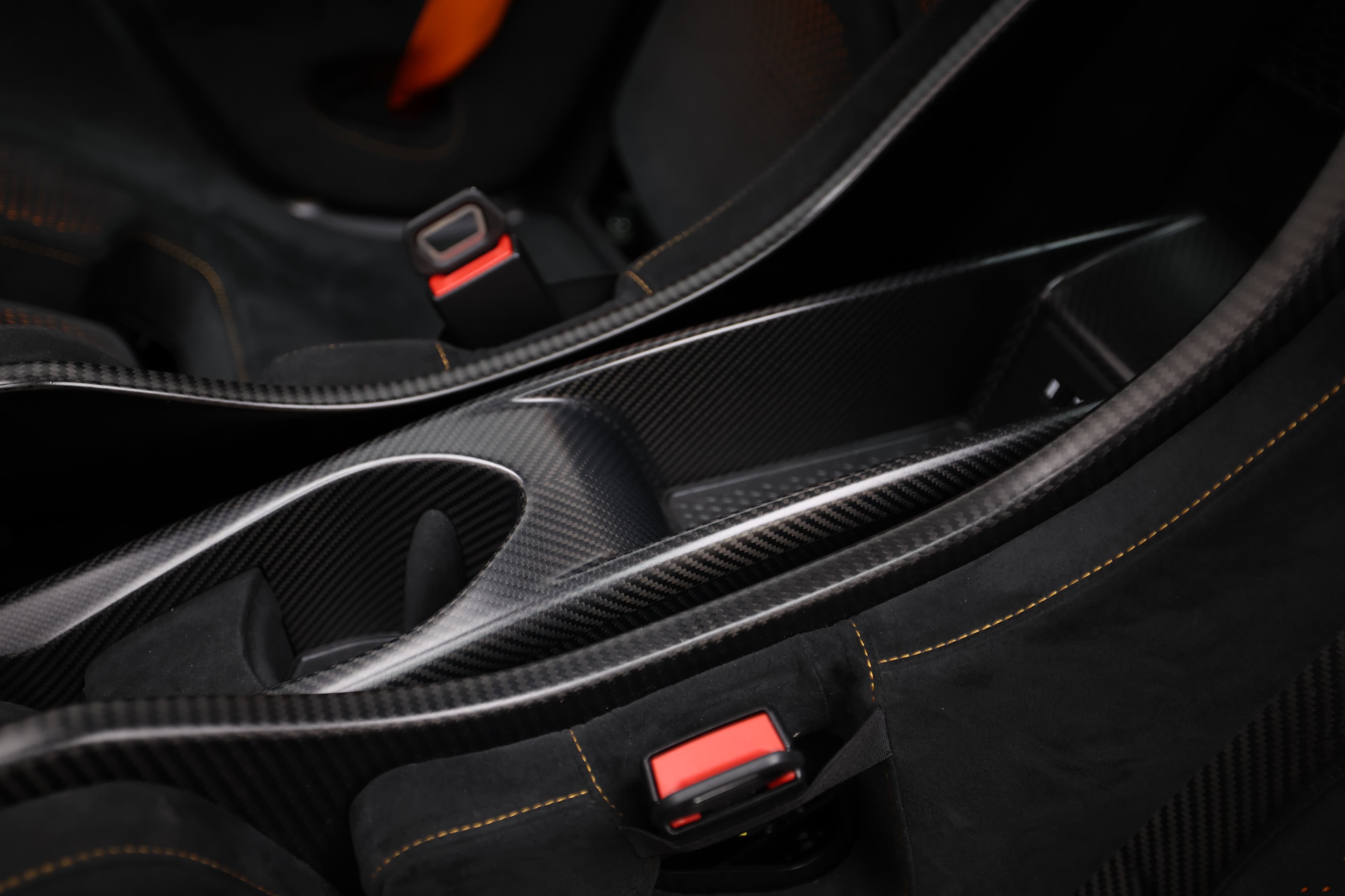 Gros plan sur le tunnel central de la McLaren 765LT, mettant en avant les éléments en carbone et les détails en rouge, soulignant la sportivité et le design raffiné de l'habitacle.