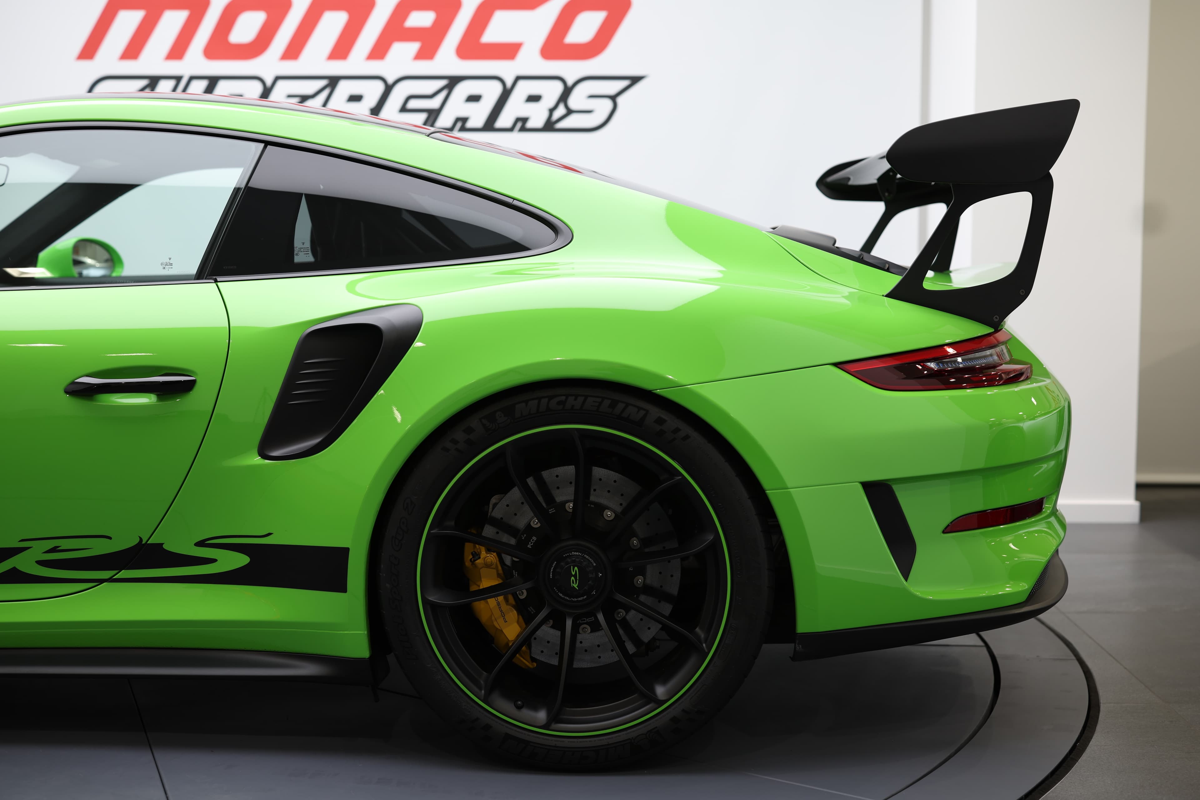Vue arrière trois-quarts de la Porsche 911 GT3 RS 991 verte, mettant en évidence l’énorme aileron fixe, les prises d’air latérales, les jantes noires cerclées de vert et le caractère résolument piste du modèle.