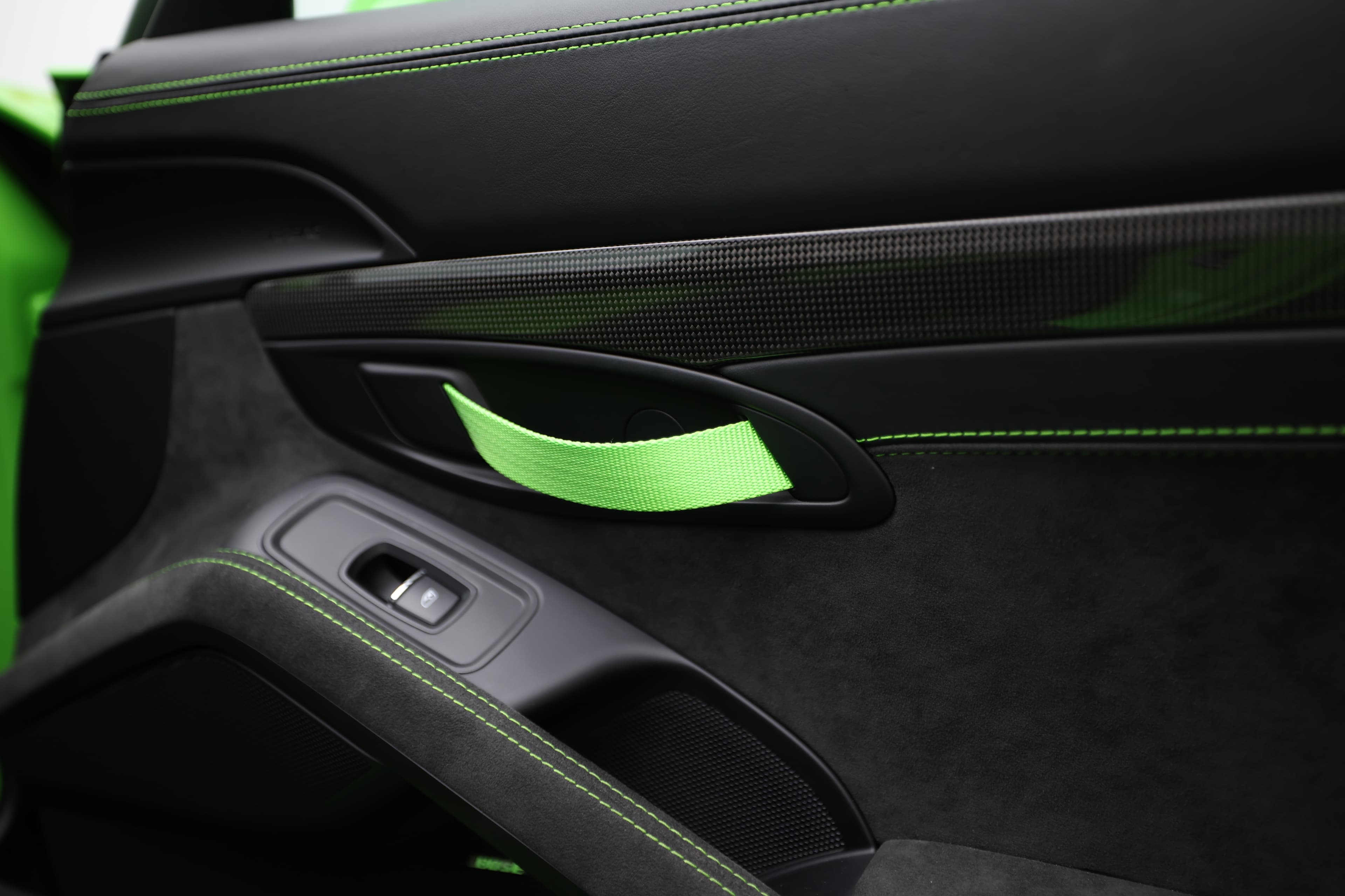 Le détail de la poignée de la porte de la Porsche GT3 RS, accentué par des finitions en carbone et des surpiqûres vertes, illustre l'attention portée à chaque élément de design, combinant élégance et sportivité.