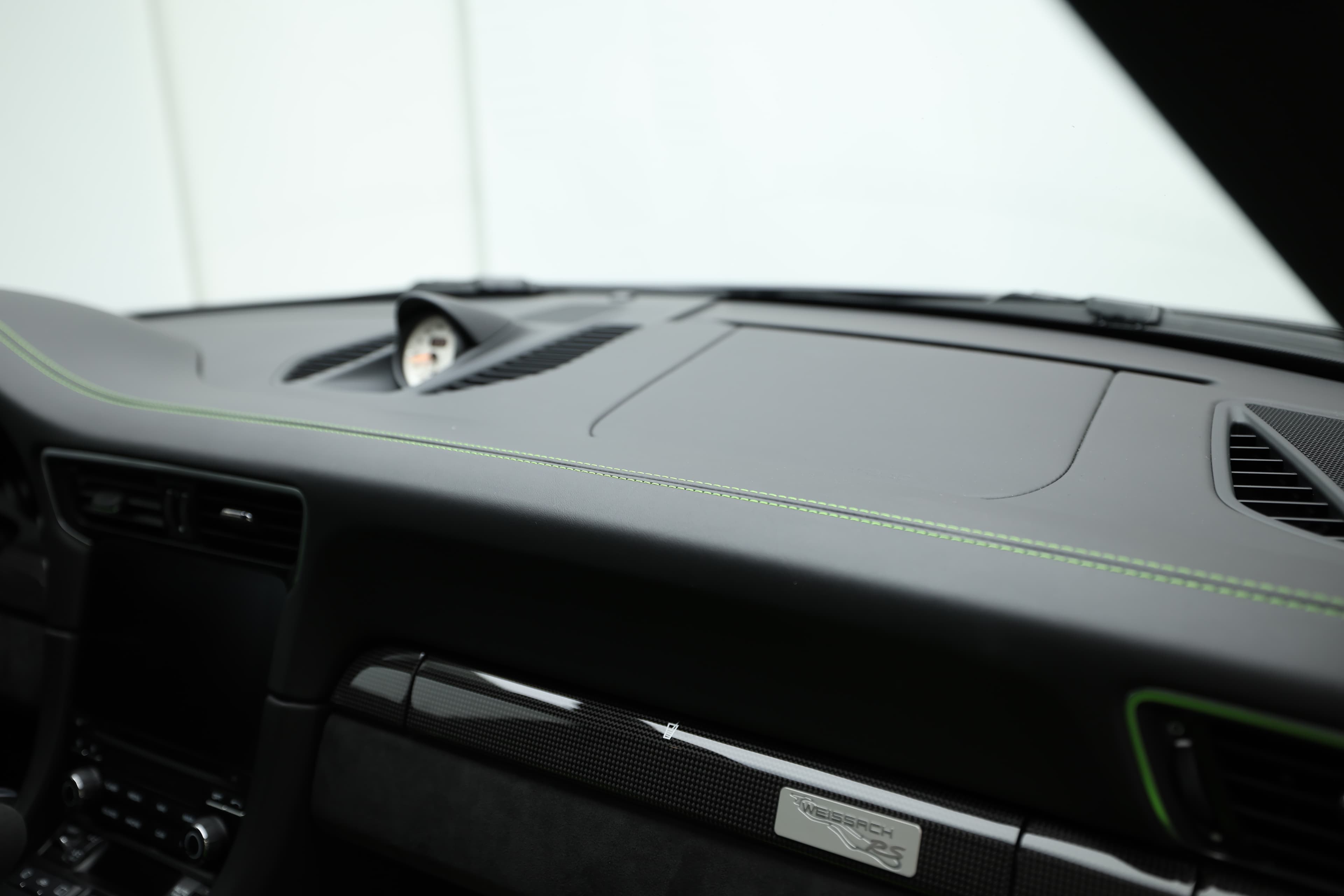 Le tableau de bord de la Porsche GT3 RS, avec ses finitions en carbone et ses accents verts, allie technologie moderne et design sportif, créant un environnement de conduite à la fois élégant et fonctionnel.