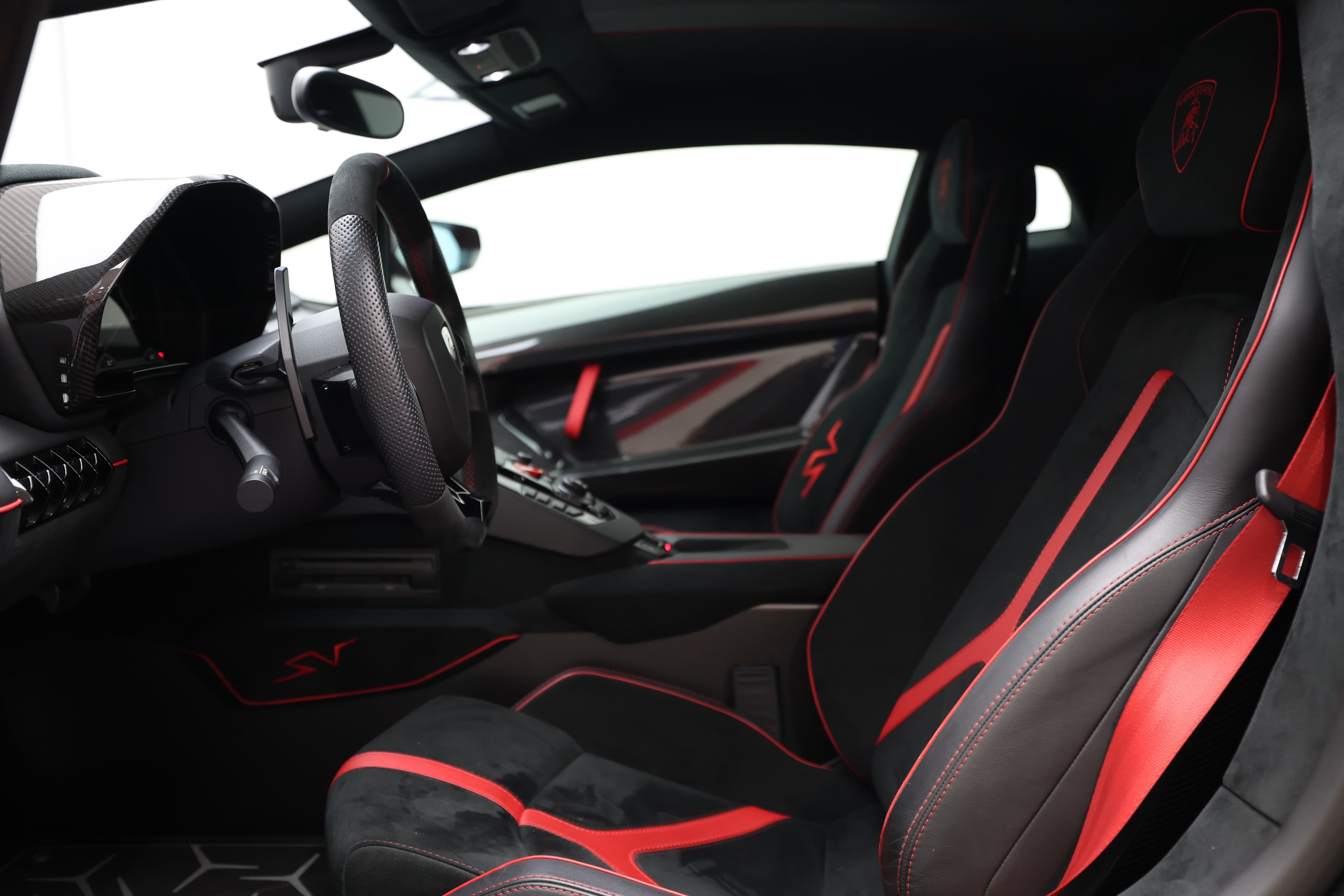 Découvrez l'intérieur de la Lamborghini Aventador SV, où le luxe rencontre la performance. Les sièges sport en cuir noir et rouge offrent un confort optimal tout en maintenant une esthétique résolument sportive, complétée par un tableau de bord orienté vers le conducteur.
