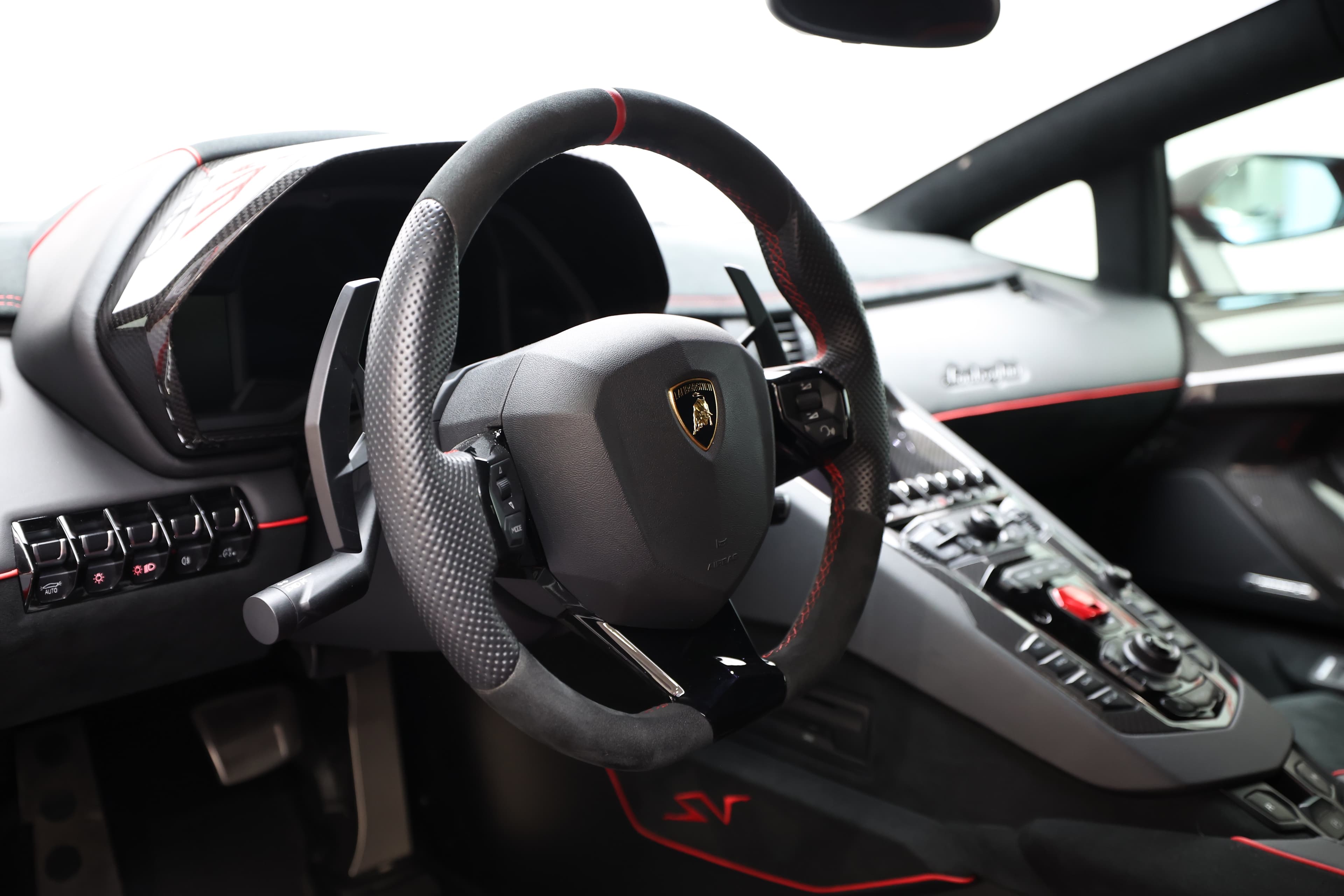 Détail du volant de la Lamborghini Aventador SV, enveloppé de cuir et de carbone, offrant une prise en main optimale. Les commandes intuitives et le design sportif ajoutent à l'expérience de conduite, mettant en avant l'engagement de Lamborghini envers l'innovation et la performance.