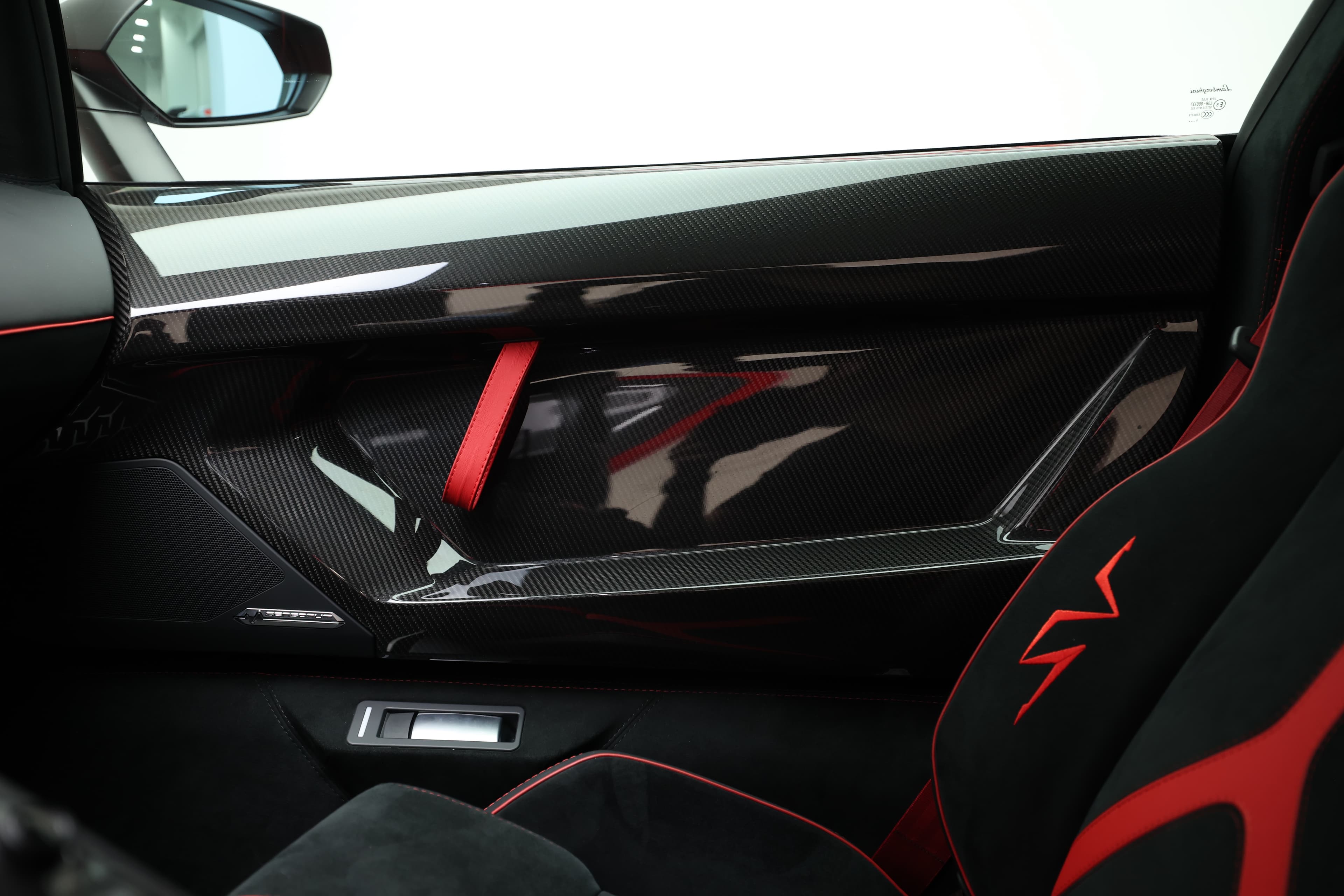 Détail de la portière de la Lamborghini Aventador SV, où le carbone et les accents rouges se marient pour créer une esthétique dynamique. Les lignes épurées et les finitions de haute qualité illustrent parfaitement le mariage entre performance et luxe, typique de Lamborghini.