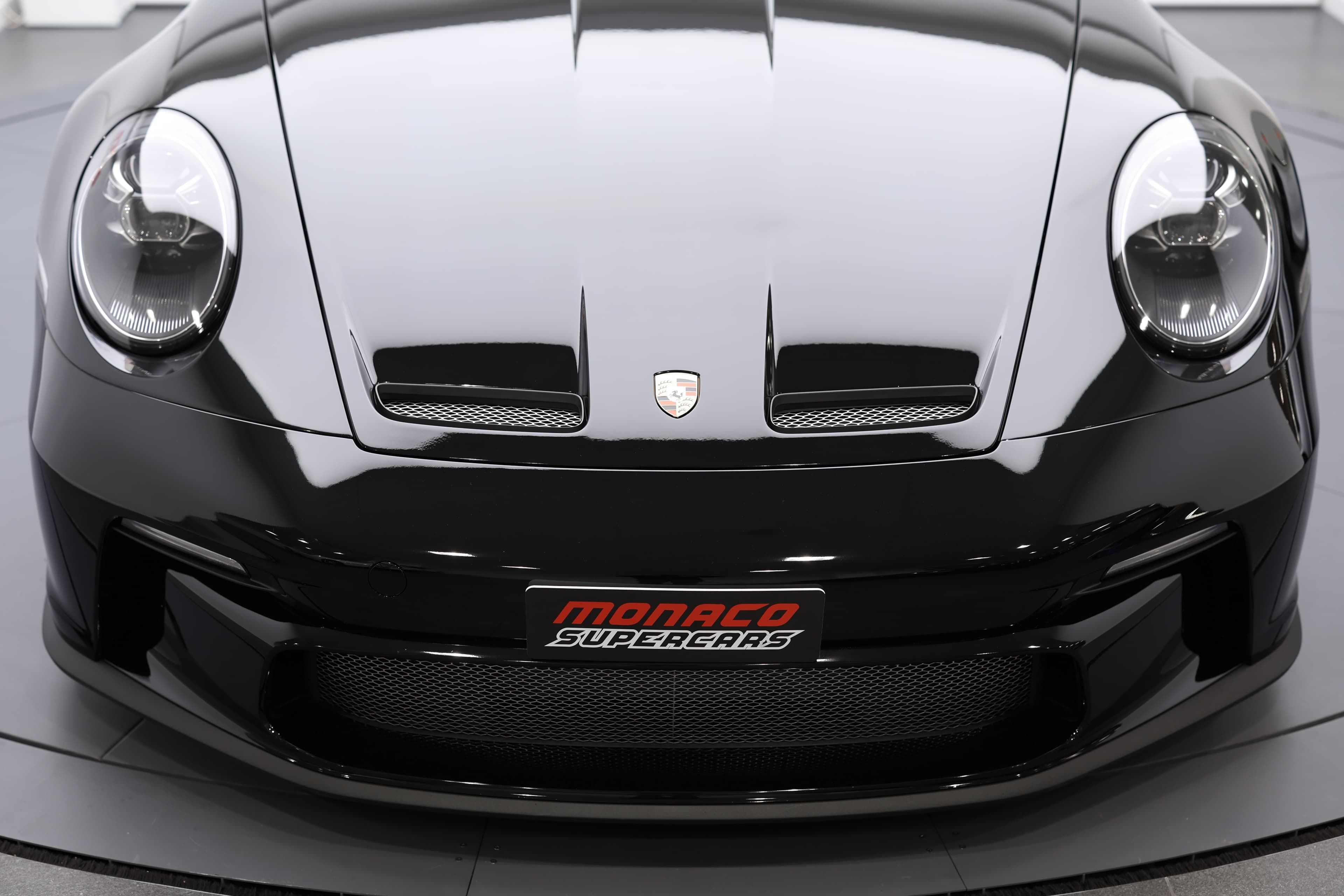 Vue de face de la Porsche 911, mettant en avant son design audacieux et sportif. Le pare-chocs agressif, les phares saisissants et le logo "Monaco Supercars" soulignent l'exclusivité et la dynamique de ce modèle, alliant performance et esthétique raffinée.