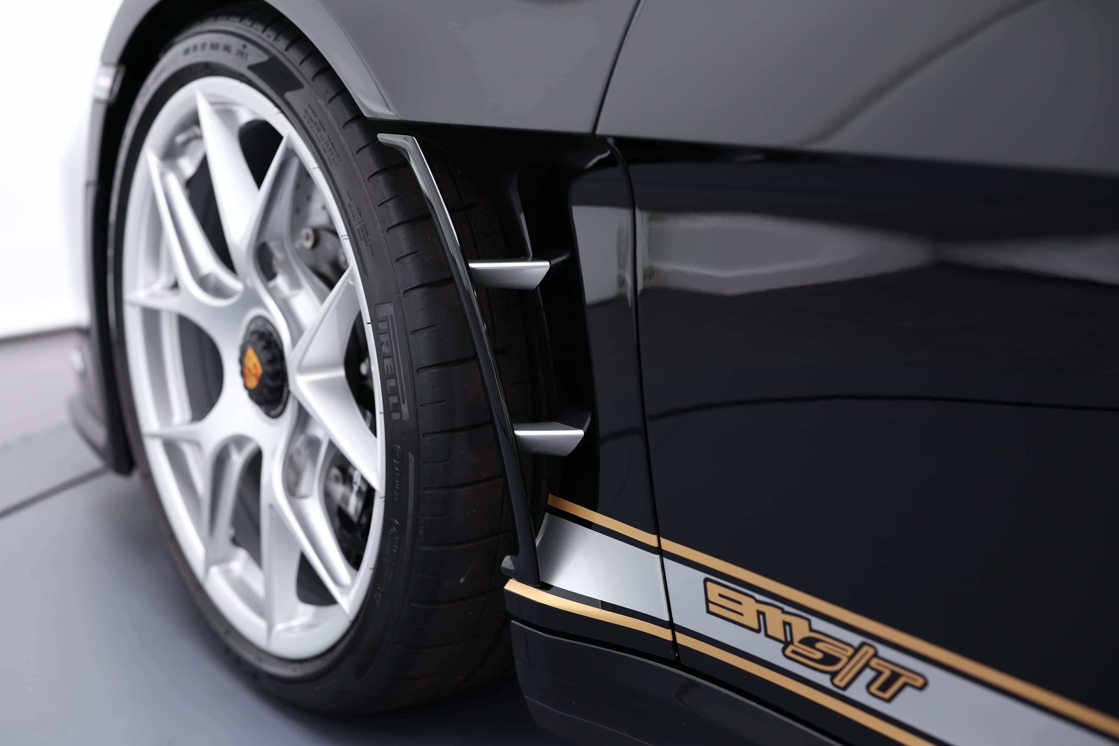 Détail sur la jante et l'aileron latéral de la Porsche 911, mettant en valeur le design dynamique et sportif du véhicule. Les jantes en alliage léger, associées aux pneus larges, renforcent non seulement l'esthétique mais améliorent également la performance sur route. Le logo "S/T" sur le bas de caisse souligne l'identité unique et l'héritage de ce modèle emblématique.