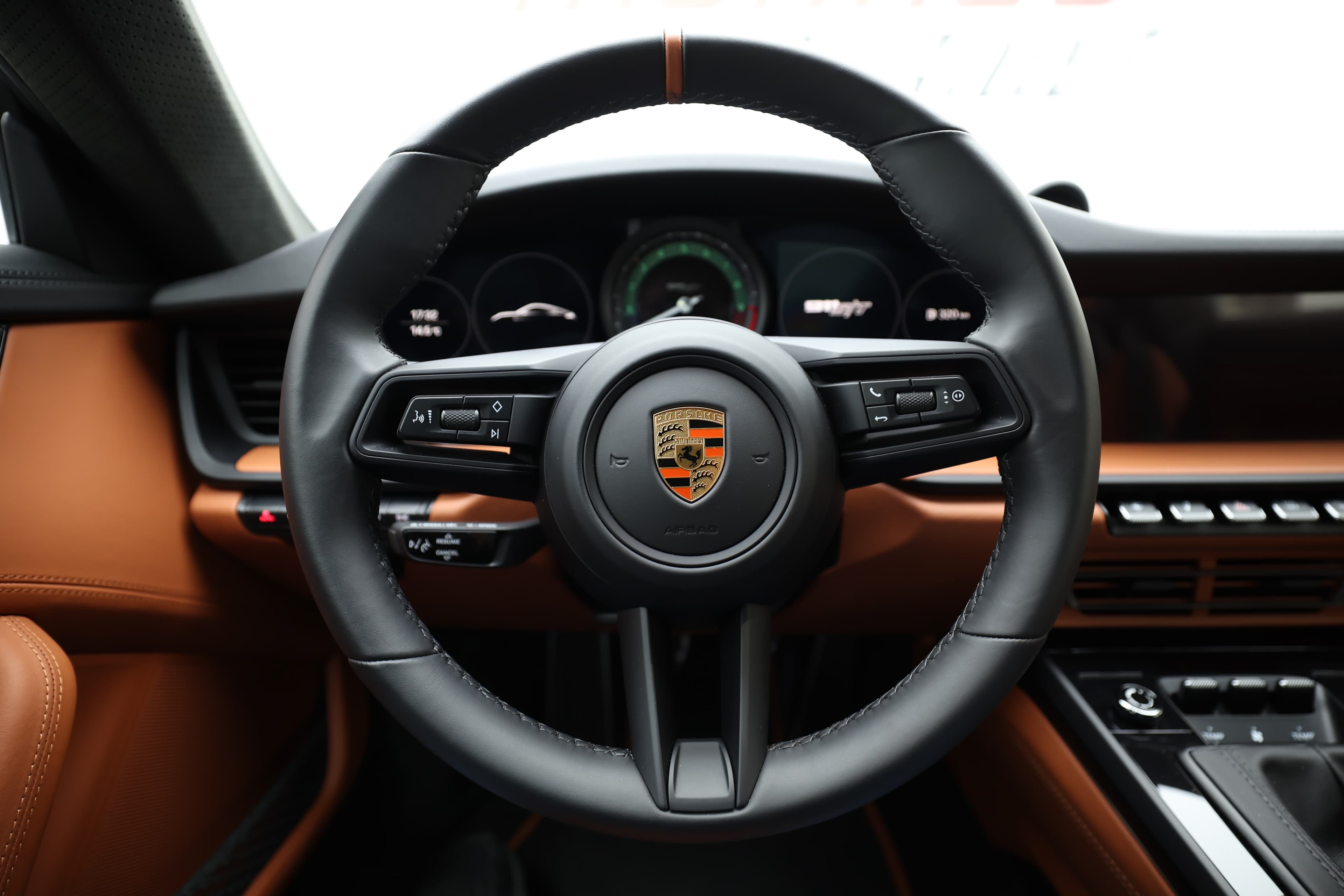 Vue de l'intérieur de la Porsche 911, mettant en avant le volant sport. Ce volant, avec sa forme ergonomique et ses commandes intégrées, offre une prise en main optimale pour une expérience de conduite dynamique. L'harmonie entre le cuir de haute qualité et les accents sportifs dans l'habitacle reflète le luxe et la performance qui caractérisent cette voiture emblématique.